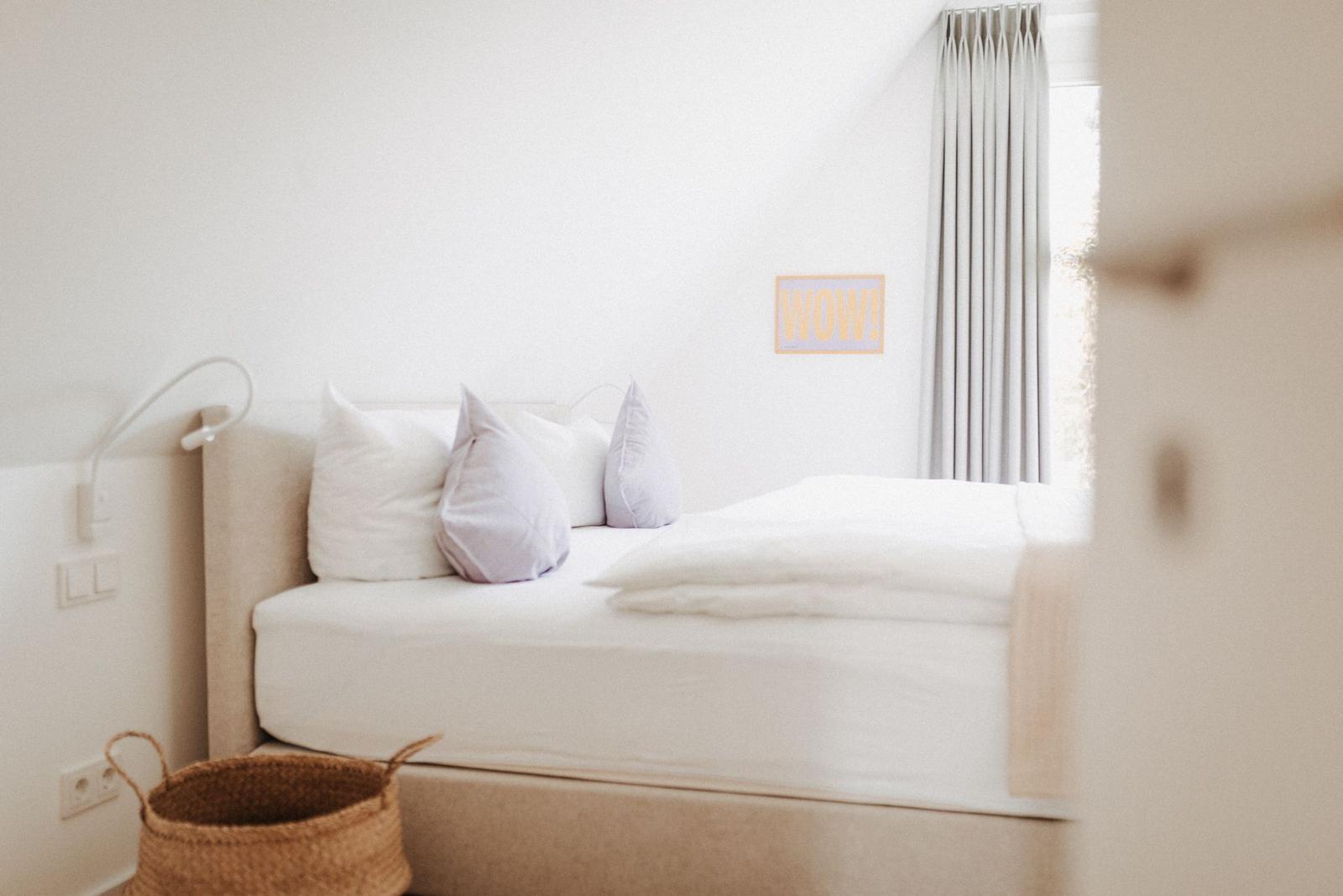 Schlafzimmer mit weißem Bett, grauen Vorhängen und einem Korb.