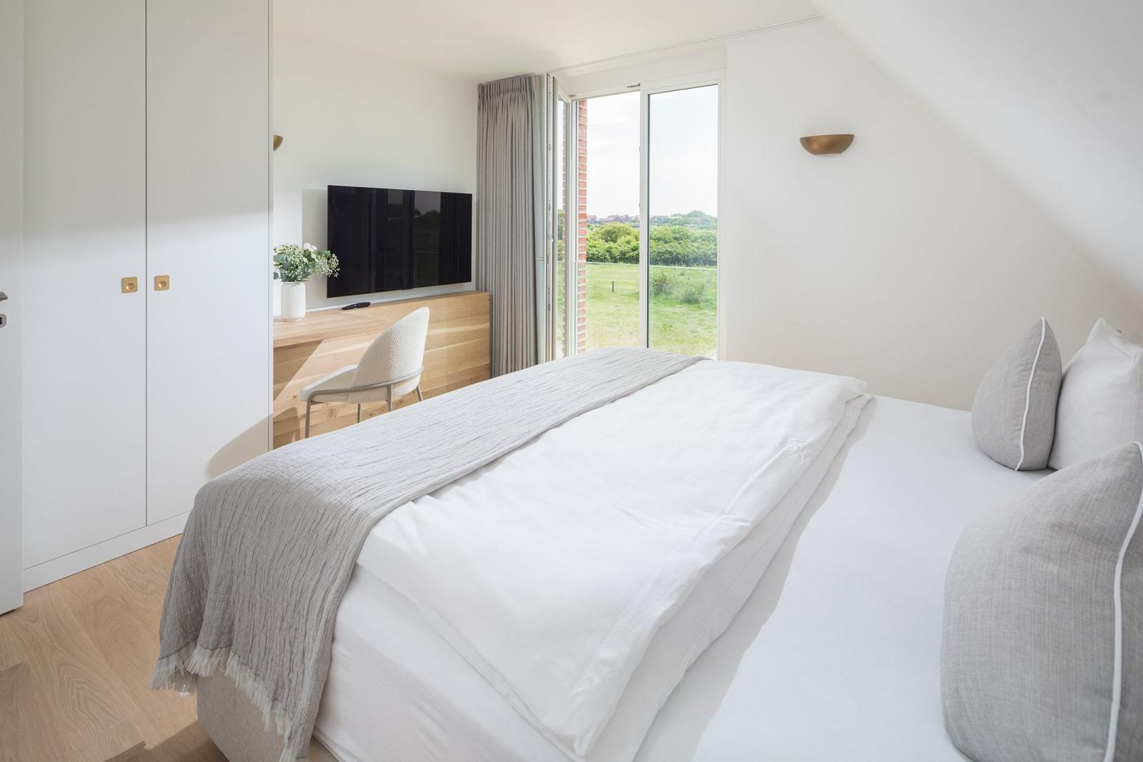 Schlafzimmer mit Doppelbett, Fernseher und Terrassentür.