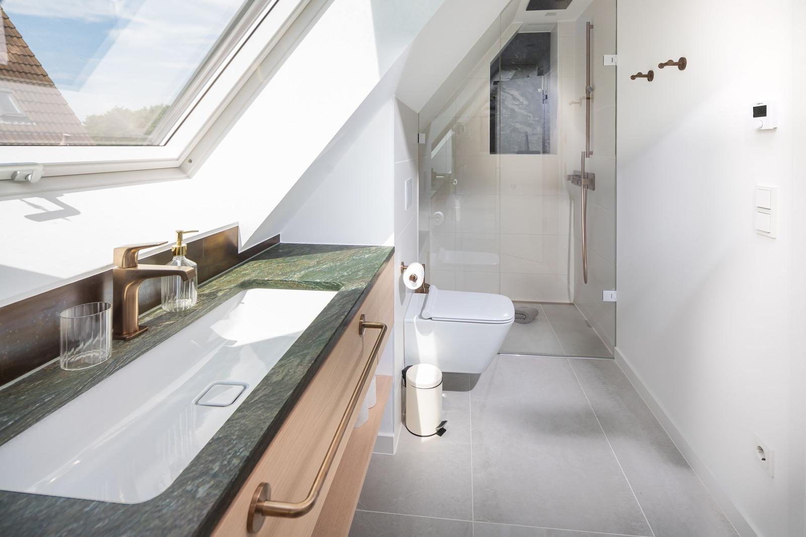 Badezimmer mit Dusche, Toilette und Waschbecken unter Dachschräge.