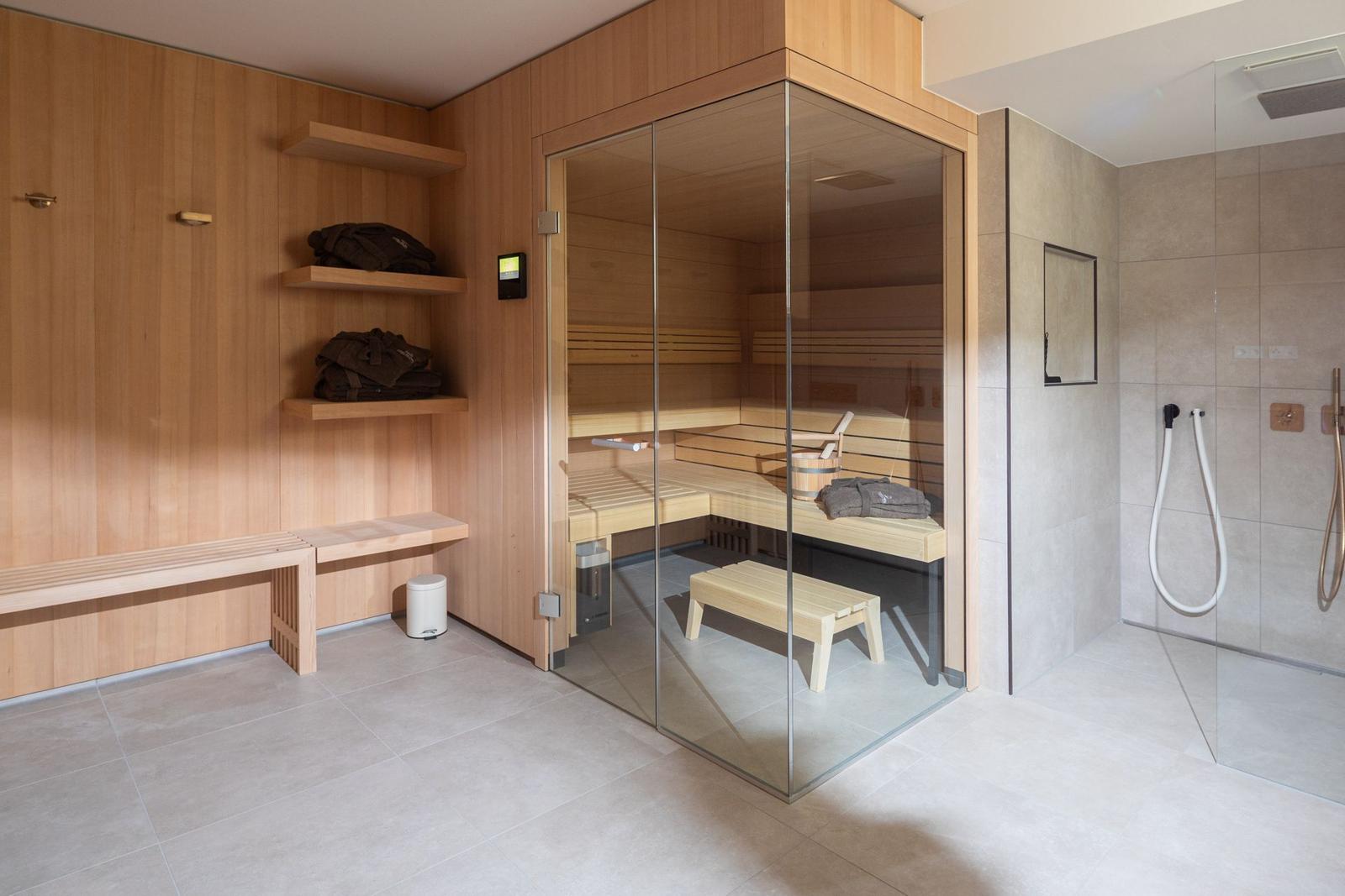 Sauna mit Glaswand, Dusche und Holzbank im Badezimmer.