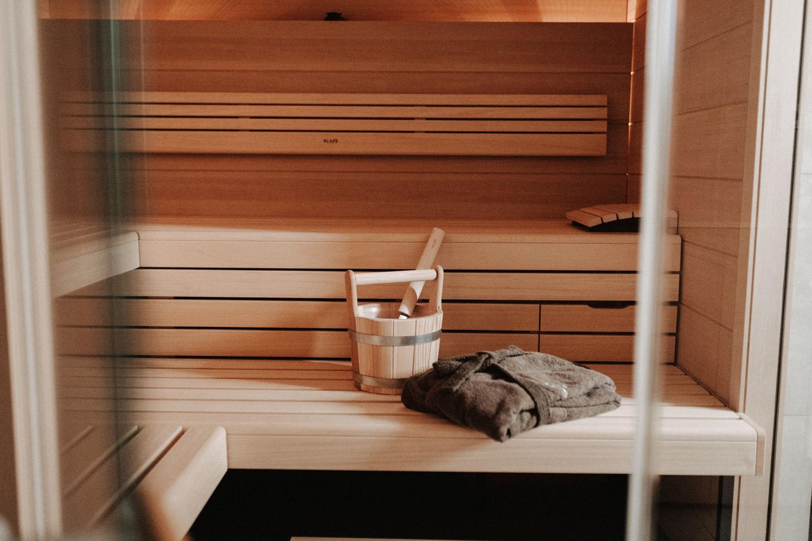 Sauna mit Holzbank, Eimer und Handtuch.