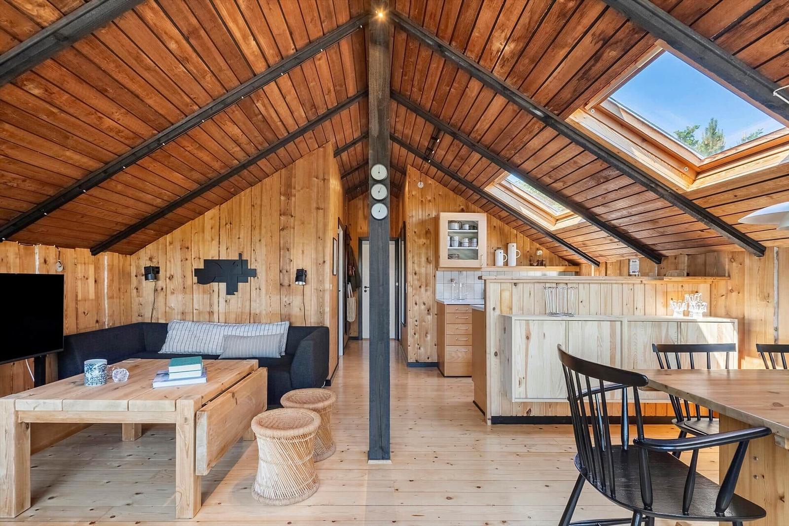 Holzverkleidete Unterkunft mit Küche, Essbereich und Wohnbereich unter Dachschrägen.
