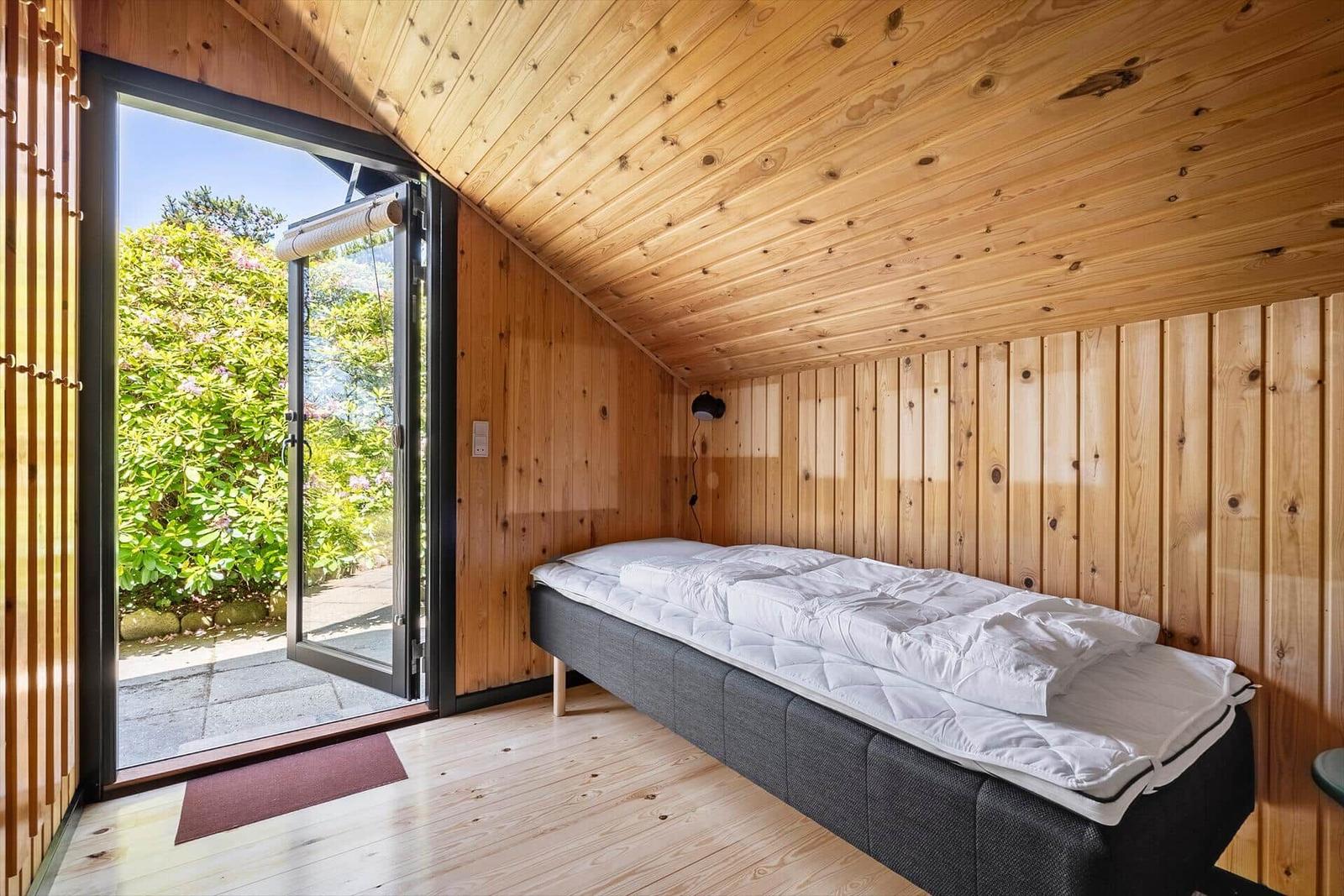 Schlafzimmer mit Bett, Holzwand und Terrassentür.