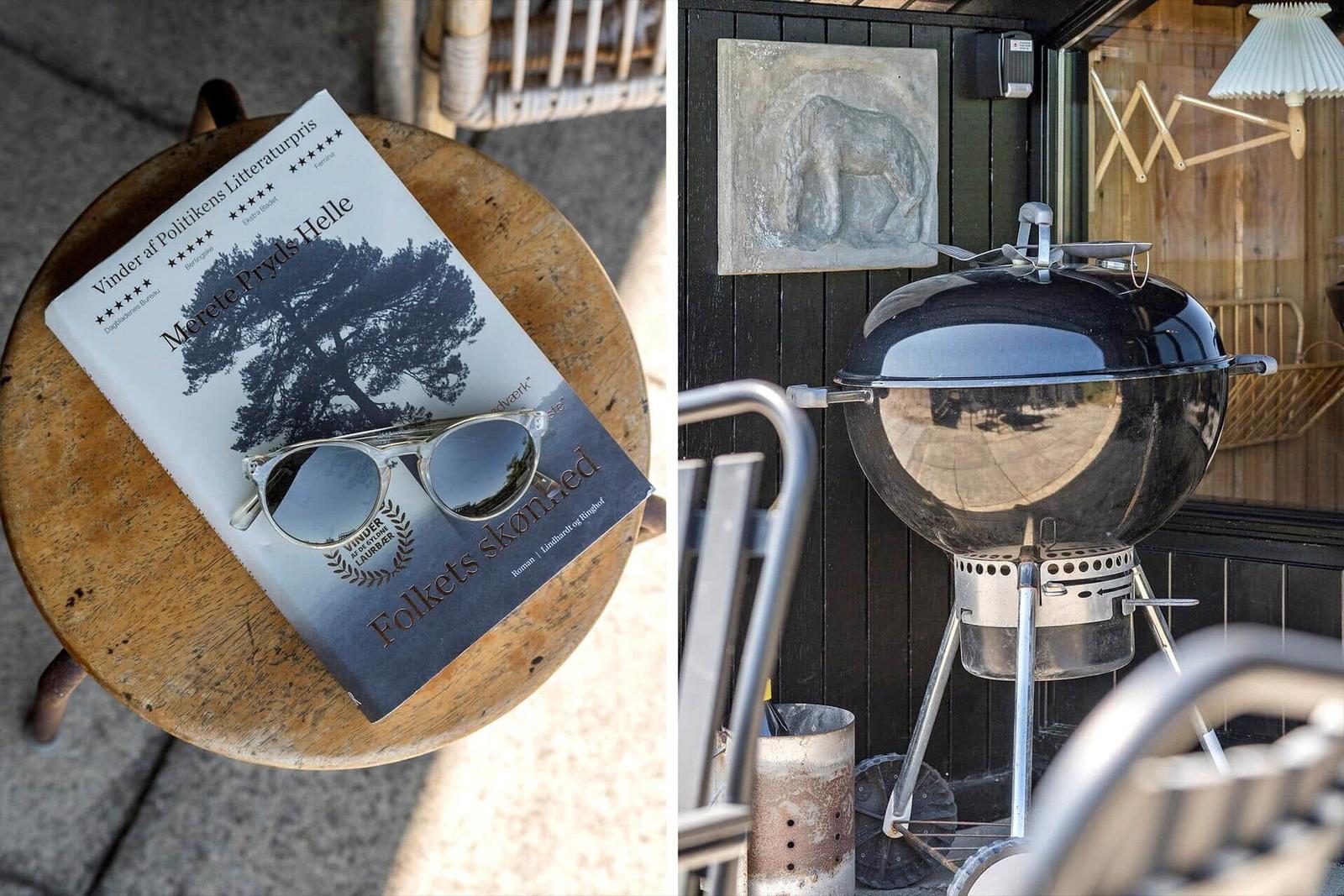 Ein Buch und Sonnenbrille auf einem Holztisch. Grill und Wandbild im Außenbereich.