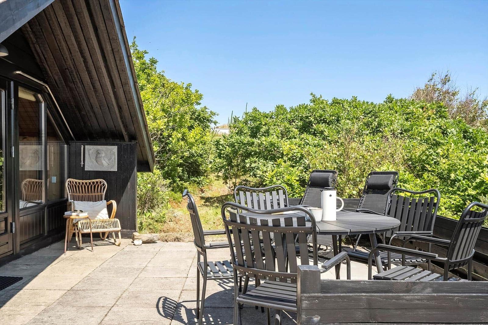 Terrasse mit Tisch, Stühlen und Blick auf grüne Vegetation.
