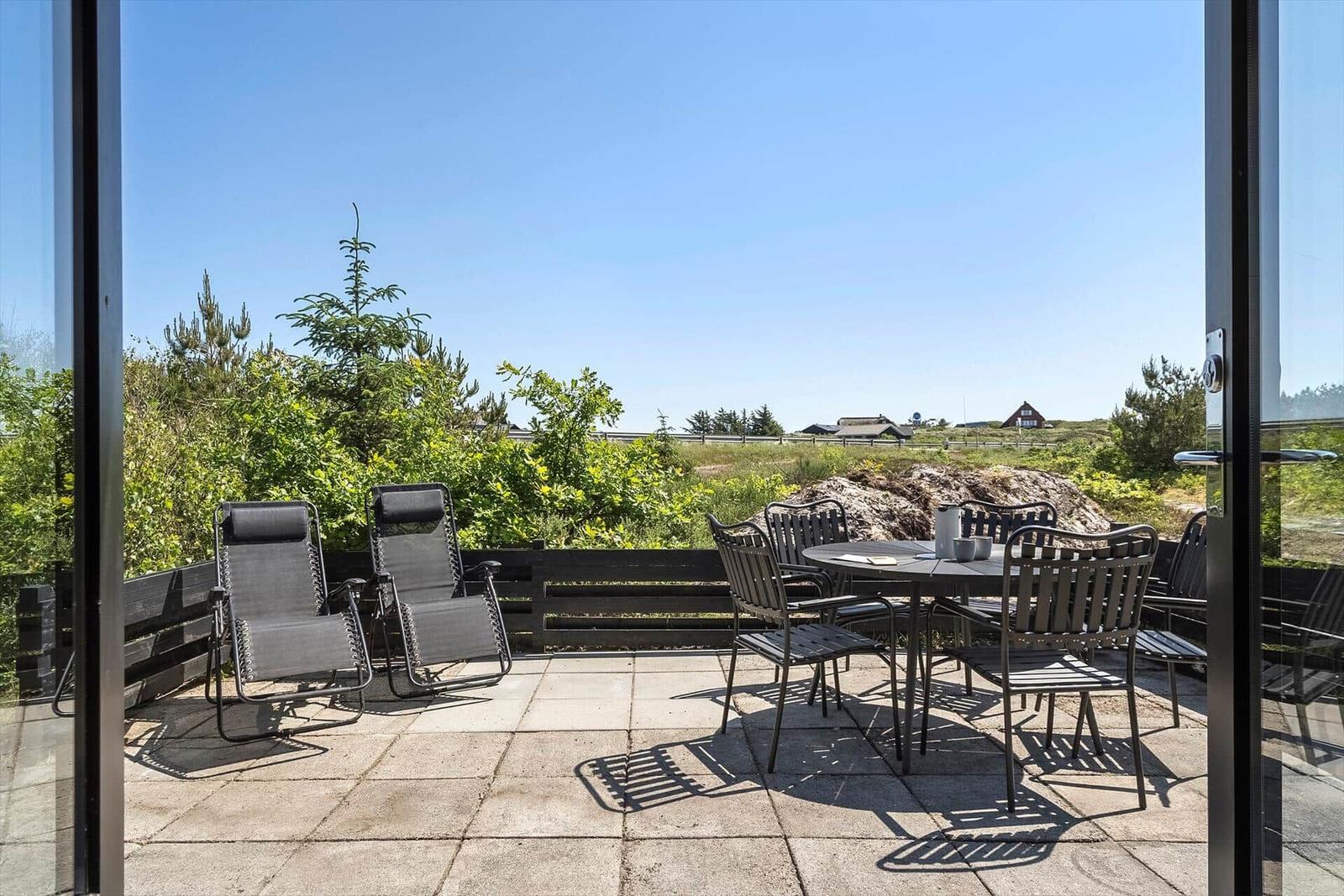 Terrasse mit Liegestühlen und Tisch für sechs Personen. Blick auf grüne Landschaft und Ferienhaus.