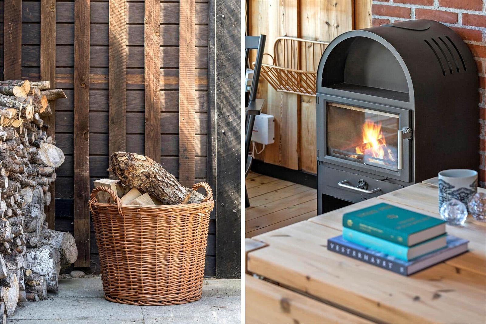 Holzstapel und Korb mit Brennholz vor Holzwand. Im Inneren brennt ein Kaminofen mit Tisch und Büchern.