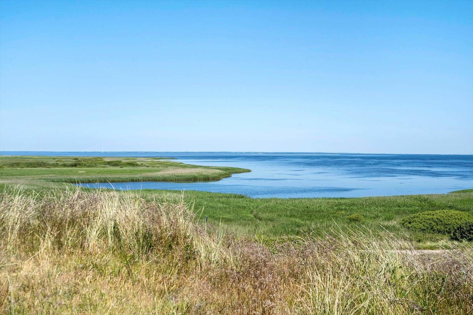 Weitläufiger Blick auf Küstenlandschaft mit Gras und Wasser unter blauem Himmel.
