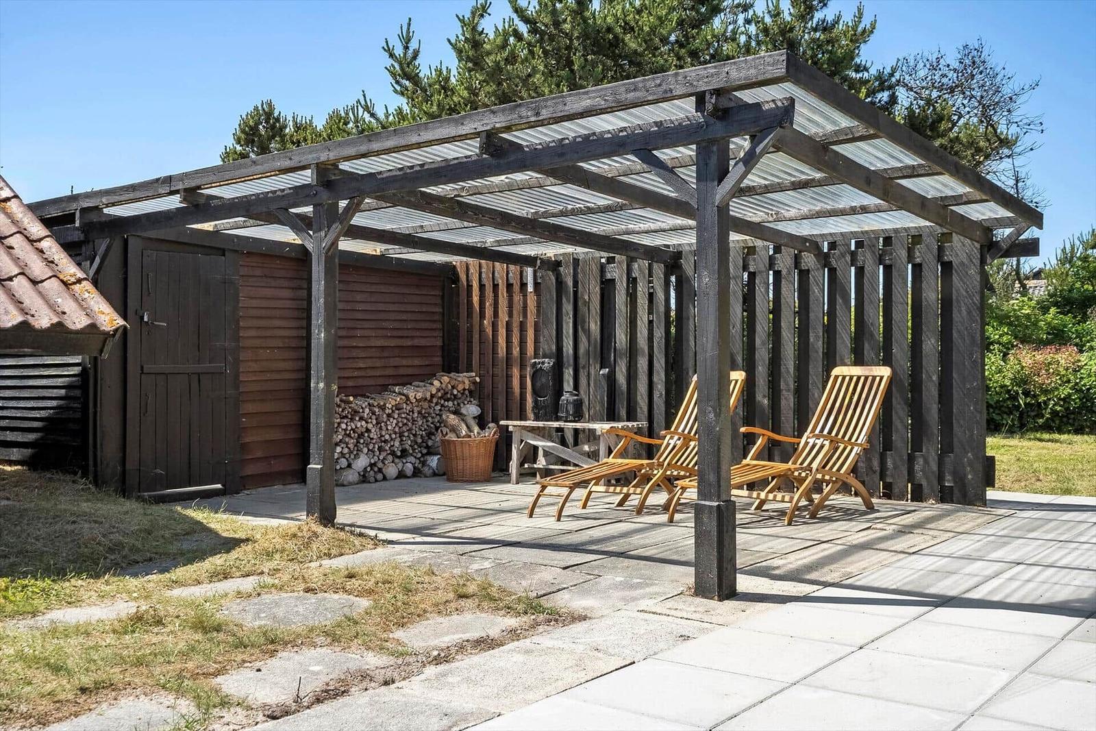Terrasse mit Holzliegen und Pavillon unter blauem Himmel.