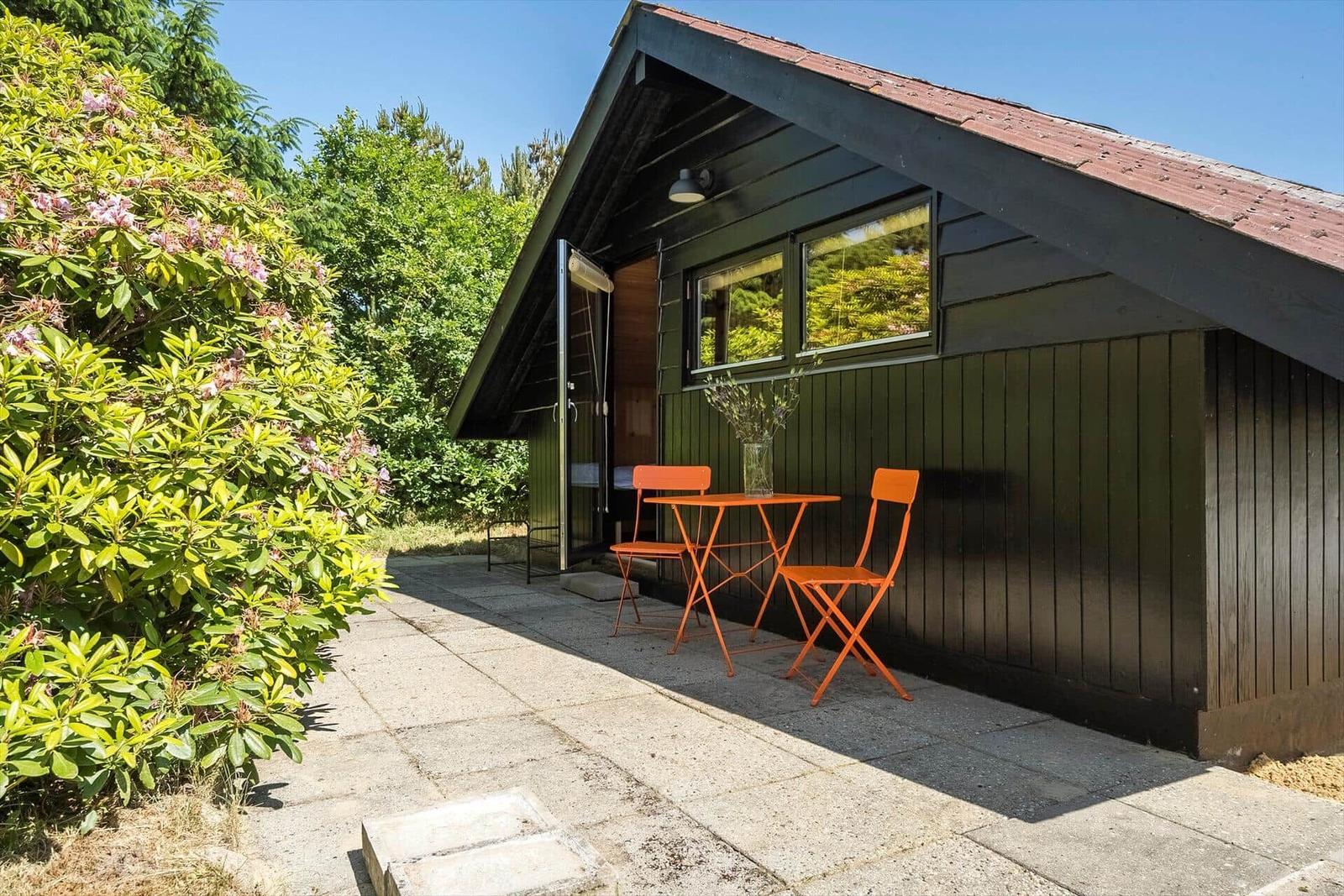 Ein kleines Haus mit einer Terrasse und orangefarbenem Tisch und Stühlen.