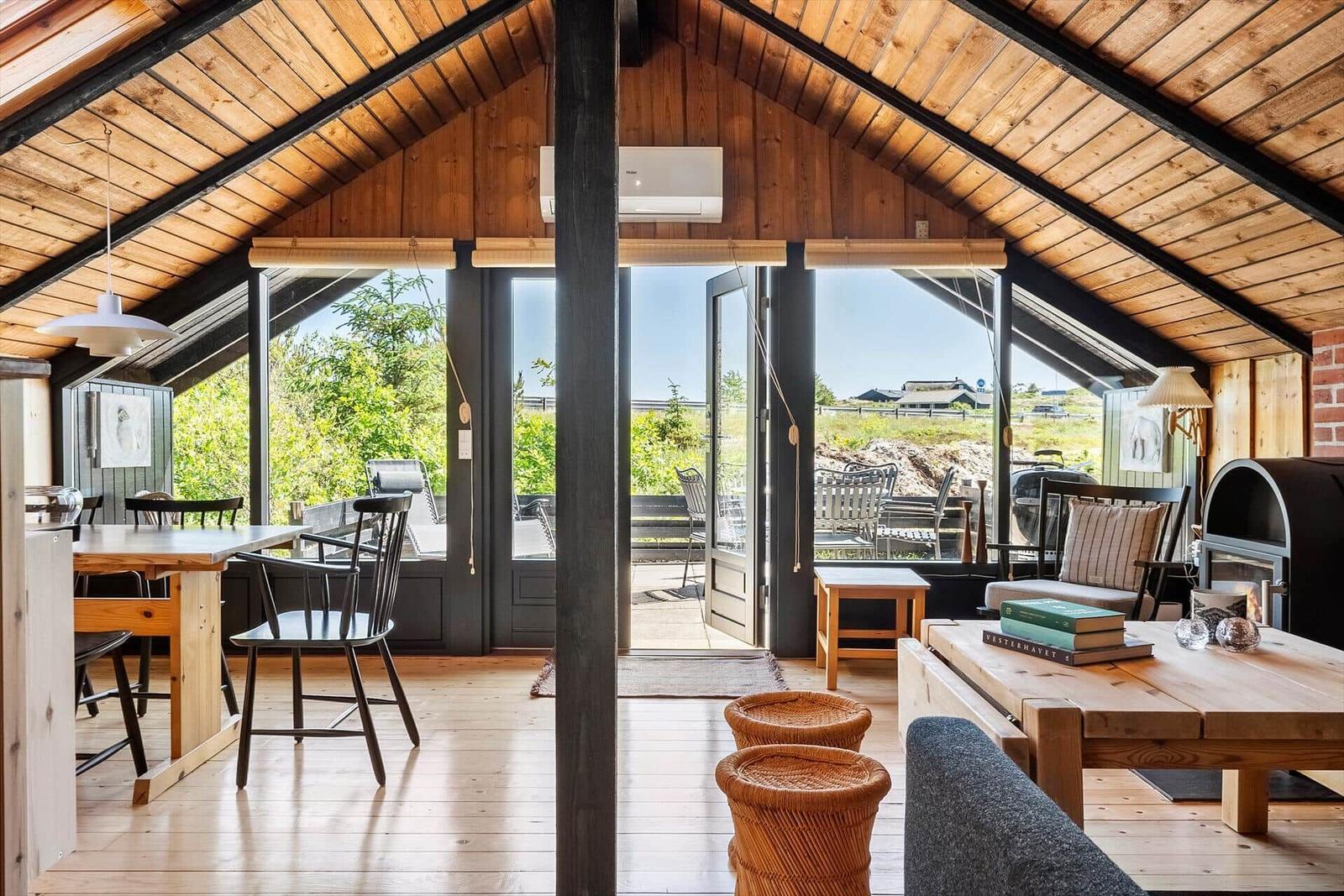 Wohnbereich mit Holzdecke, Tisch, Stühle und Blick auf die Terrasse.