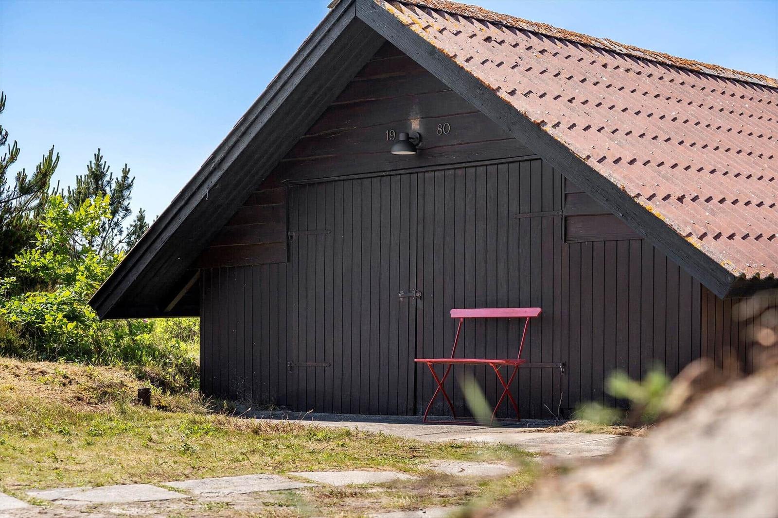 Ein dunkles Holzhaus mit rotem Dach und einer roten Stuhlbank davor.