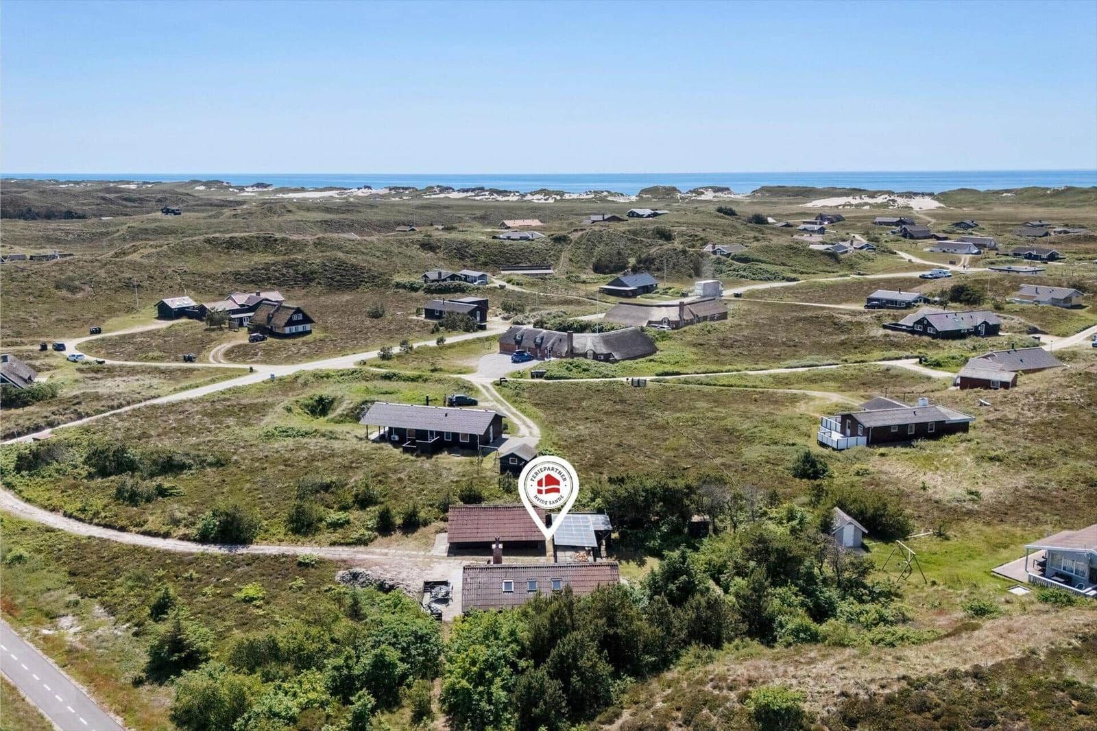 Luftbild von Ferienhäusern auf grüner Dünenlandschaft mit Blick auf das Meer.