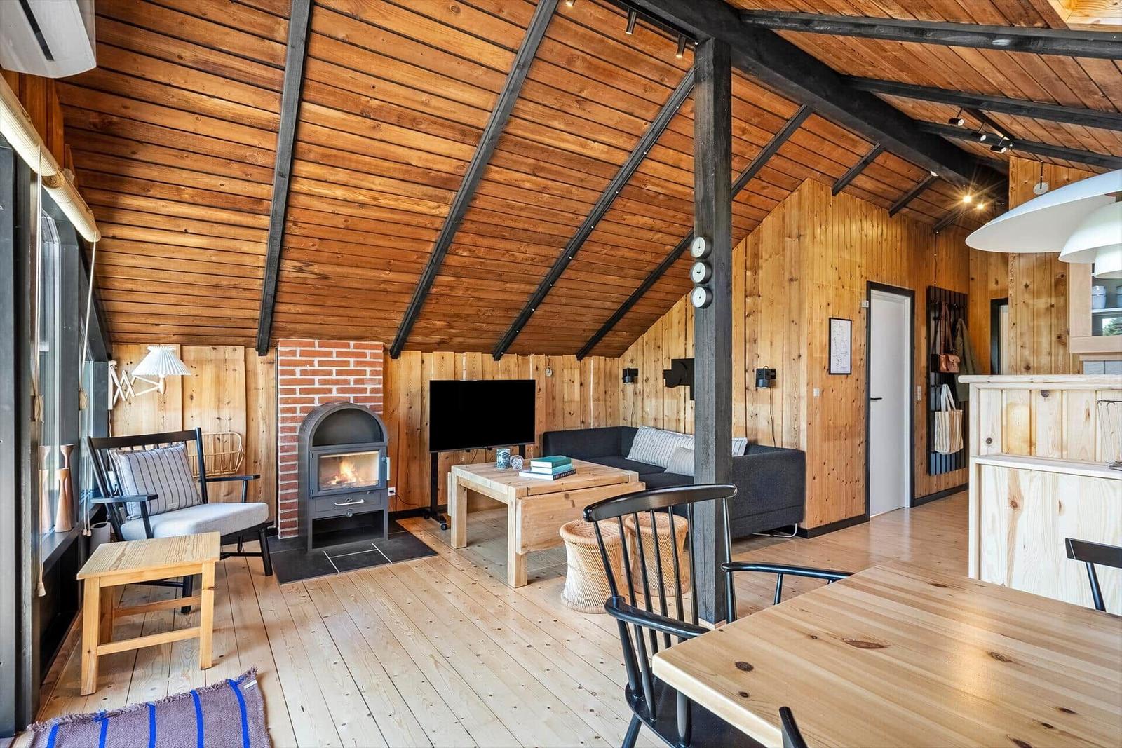 Wohnbereich mit Kamin, Sofa und Esstisch unter Holzdecke.