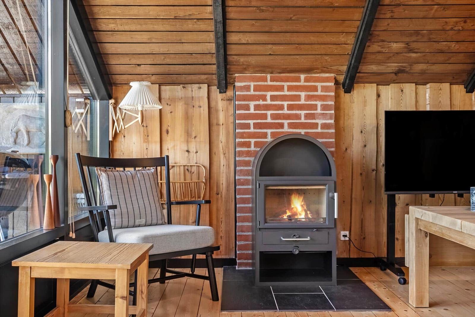 Wohnraum mit Kamin, Sessel und TV. Holzwände und Boden.