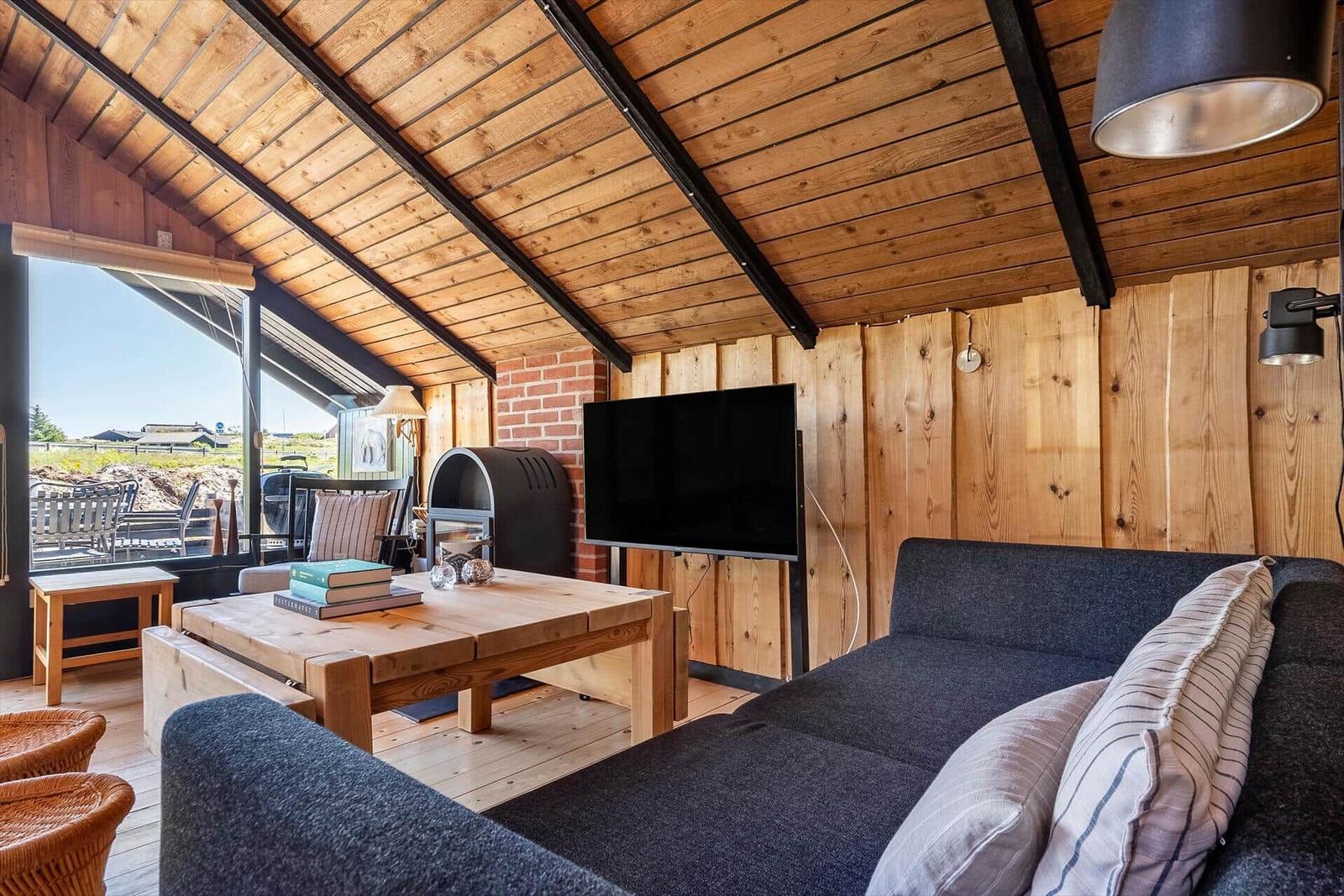 Wohnzimmer mit Sofa, Couchtisch und Fernseher unter Holzdecke.