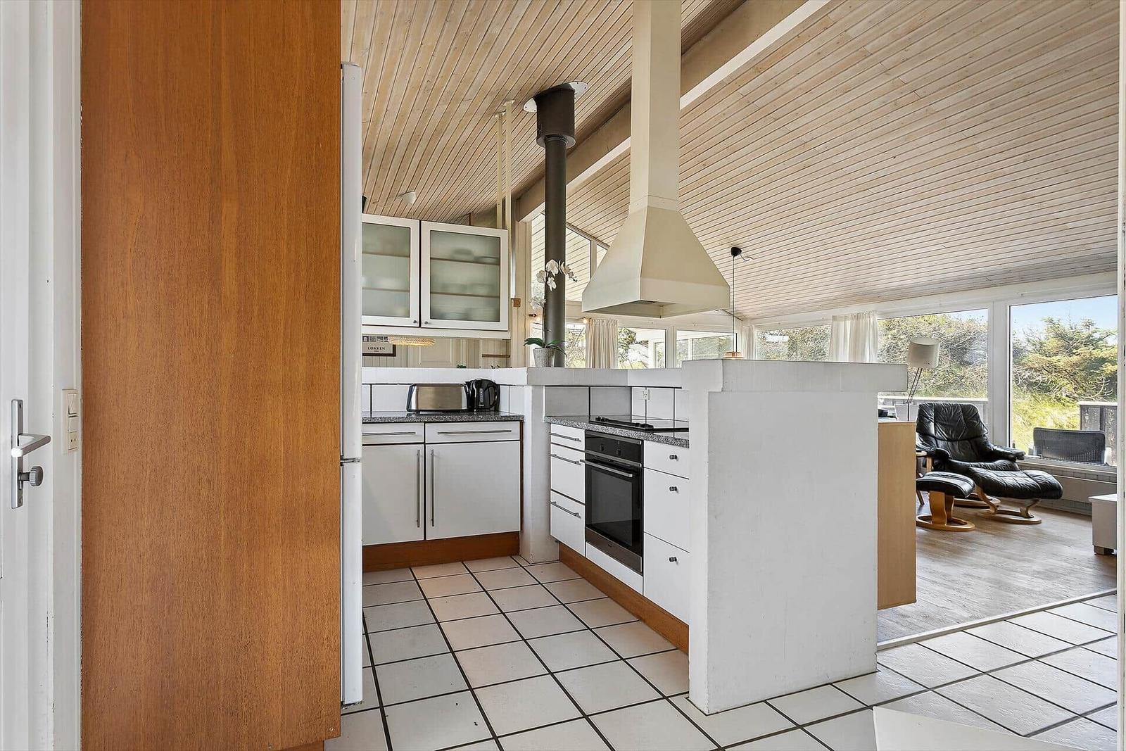 Küche mit weißer Arbeitsplatte und Holzdecke. Blick in Wohnzimmer mit Sessel.