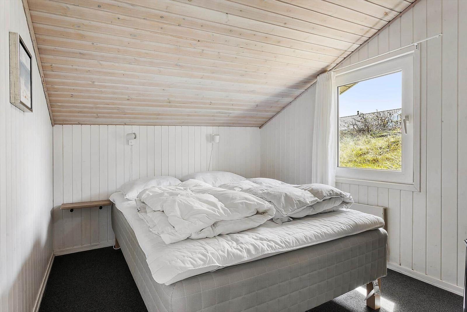 Schlafzimmer mit Doppelbett, Fenster und Holzdecke.