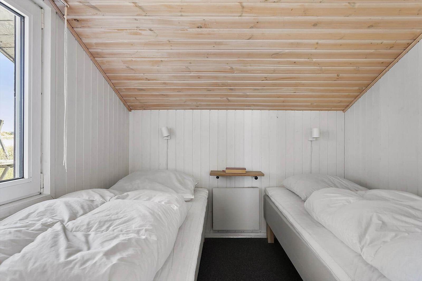 Zwei Betten mit weißen Laken, Holzdecke und Fenster. Zwischen den Betten steht ein kleiner Tisch.