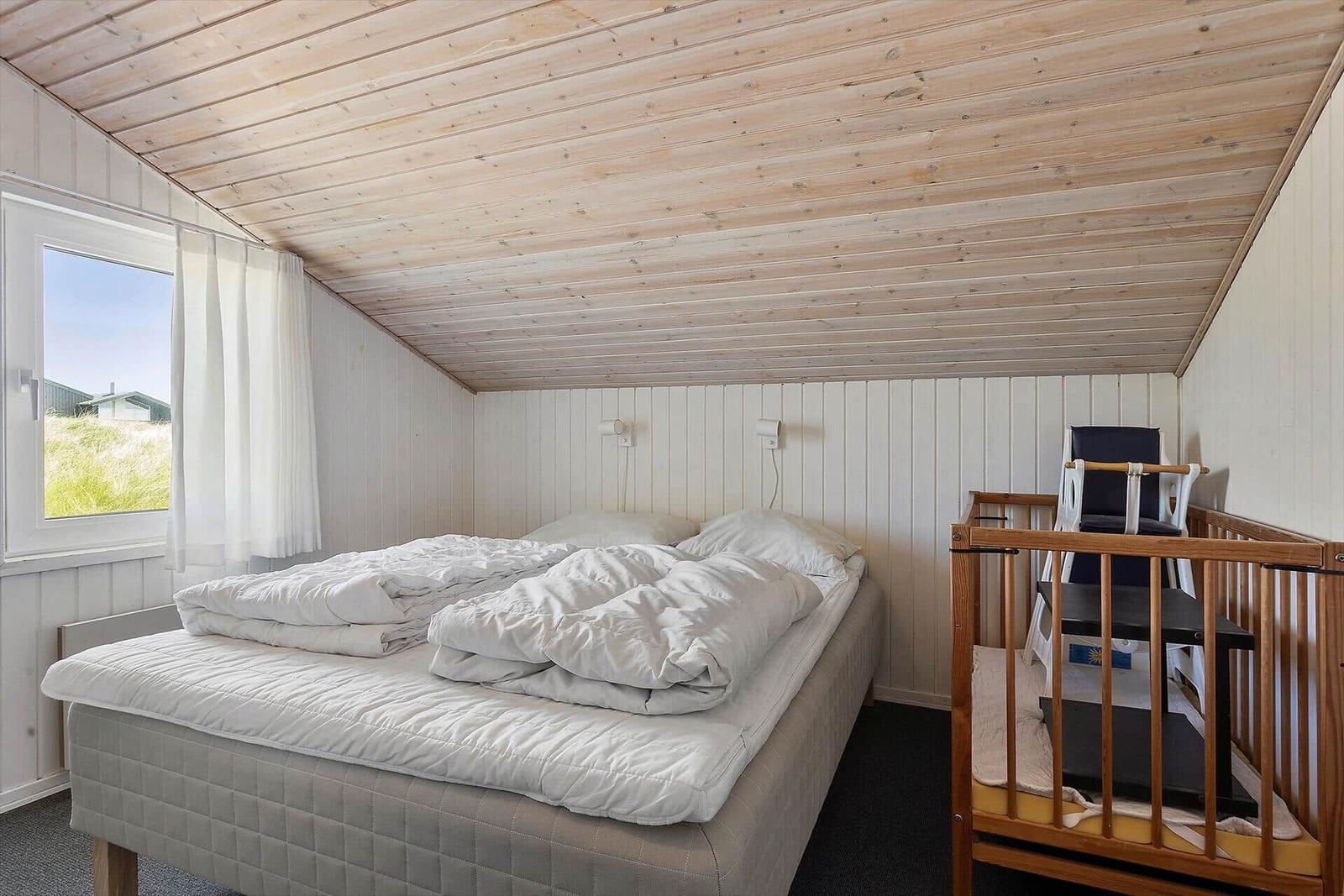 Schlafzimmer mit Bett, Kinderbett und Fenster. Holzdecke und weiße Wände.