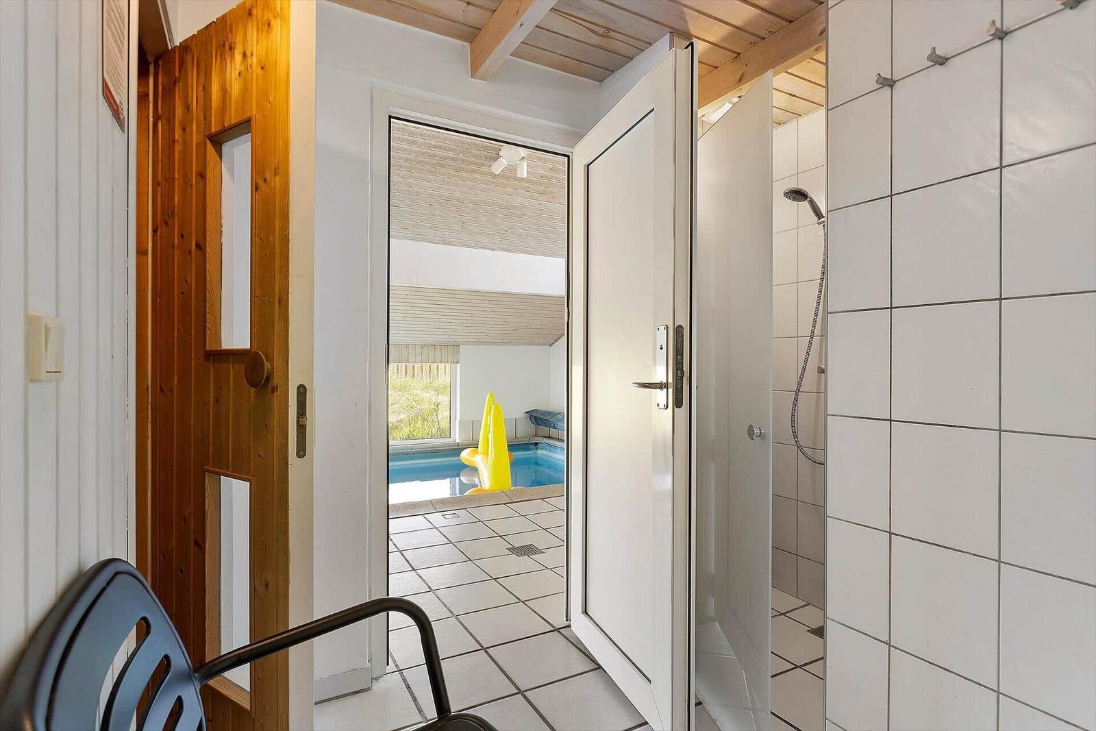 Durch die Tür ist ein Pool mit gelber Schwimmhilfe sichtbar. Rechts befindet sich eine Dusche.