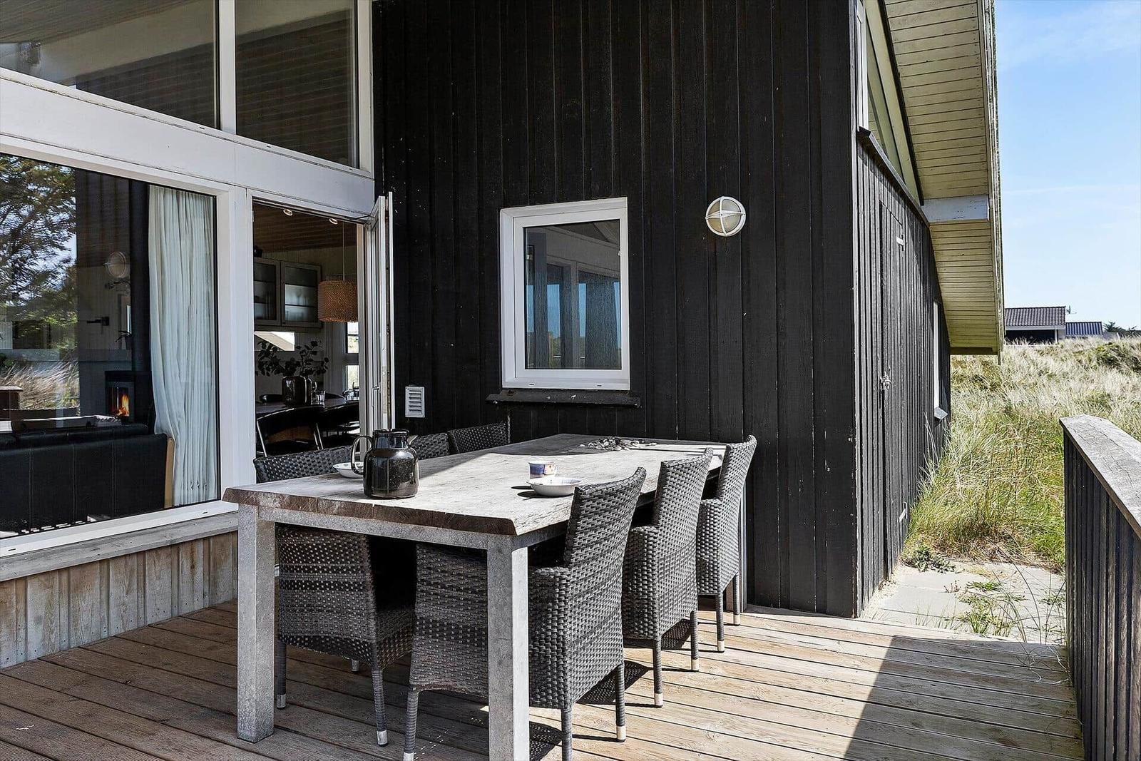 Terrasse mit Esstisch und Stühlen vor einem Haus mit dunkler Holzfassade.