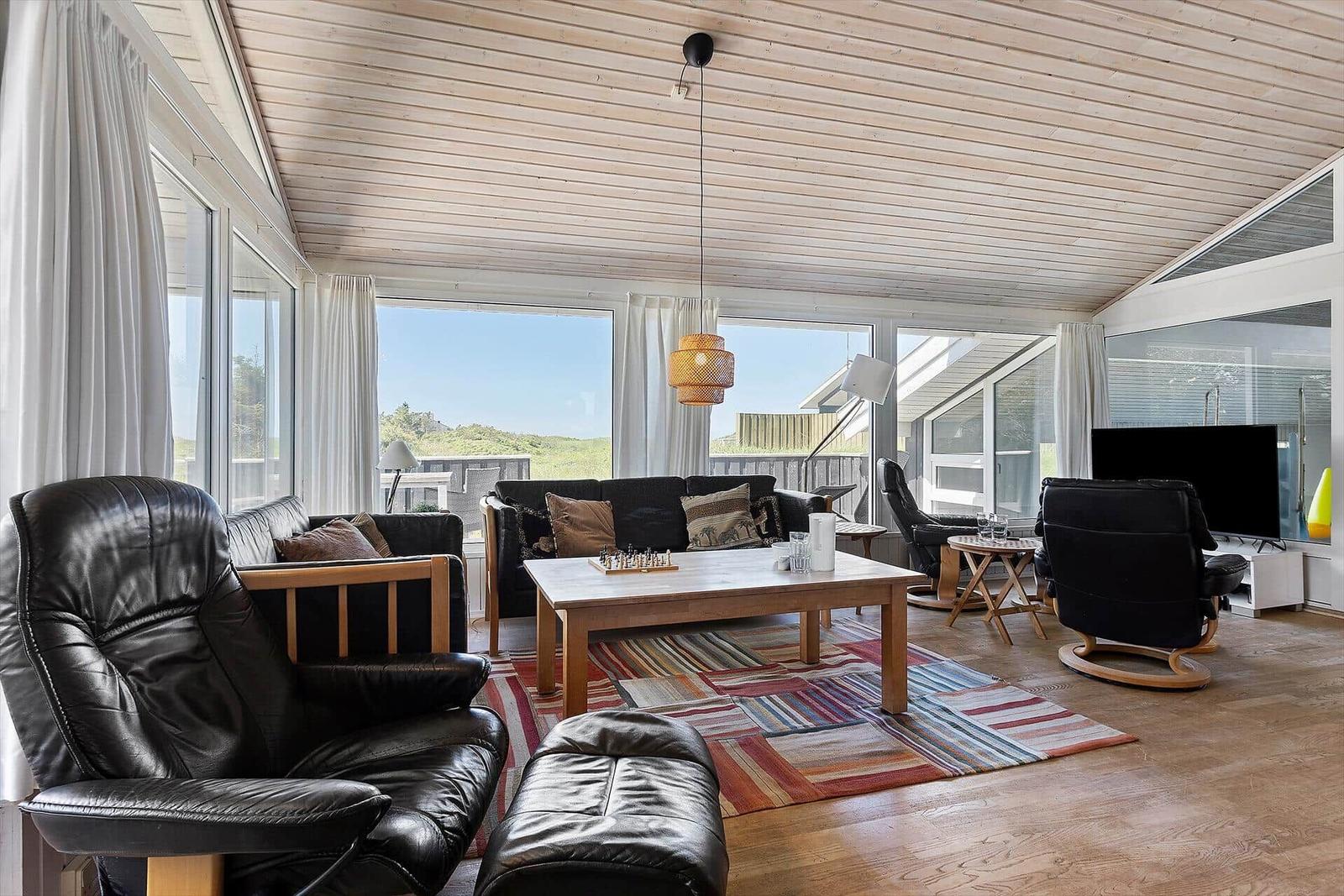 Wohnzimmer mit schwarzen Ledermöbeln, Holzboden und großem Fensterblick.