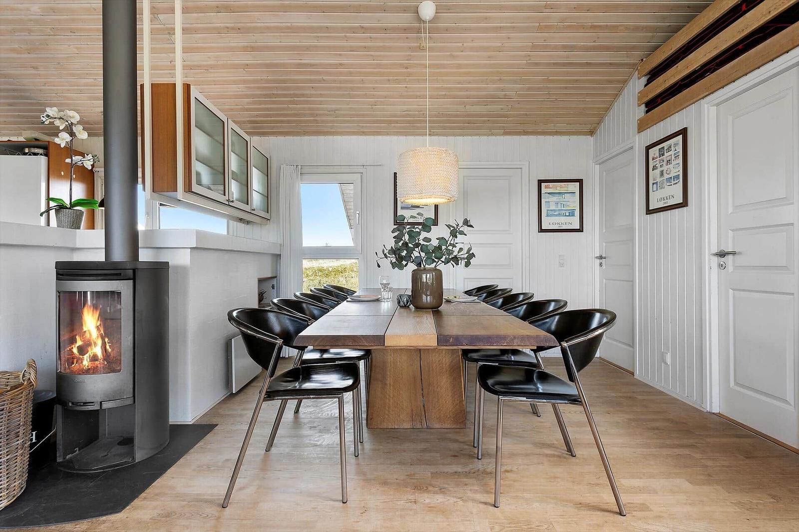 Essbereich mit langer Holztisch und schwarzen Stühlen, Kamin und Holzdecke.