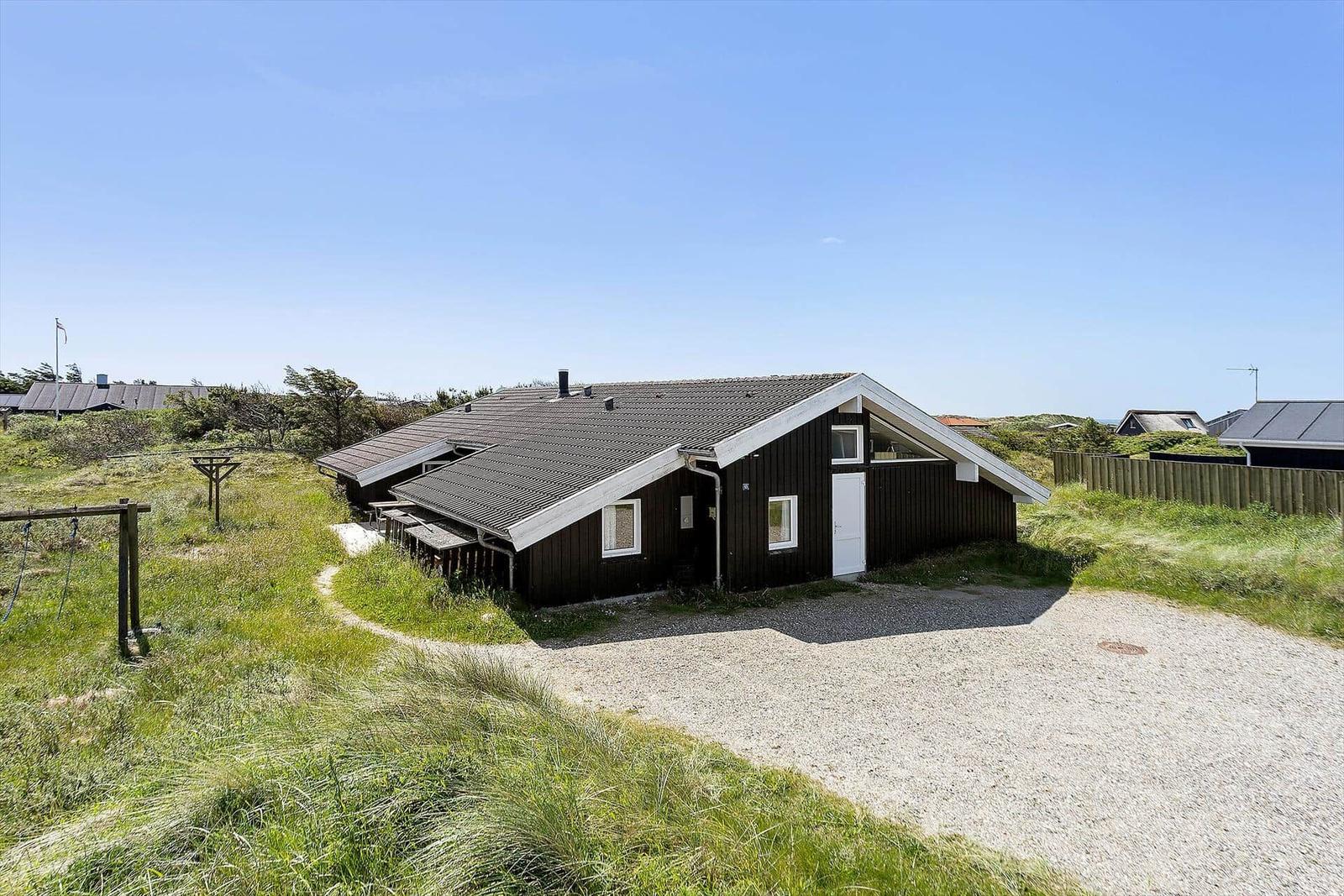 Holzhaus mit weißen Fenstern und Tür, umgeben von Gras und einem Kiesweg.