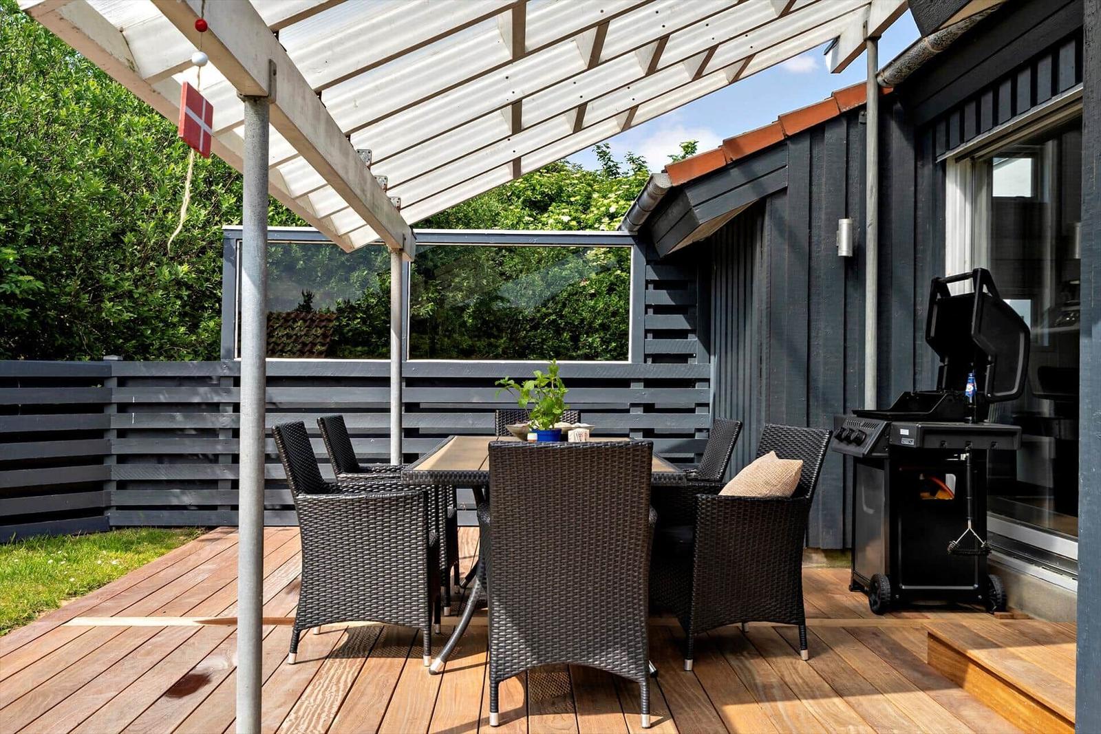 Terrasse mit Sitzgruppe, Grill und Dachüberdachung. Holzdecke und Gartenbereich.
