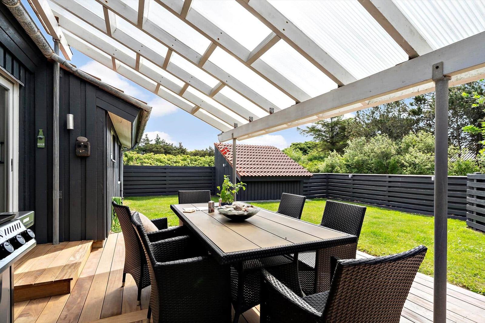 Terrasse mit Tisch, Stühlen und Grill unter Dach.