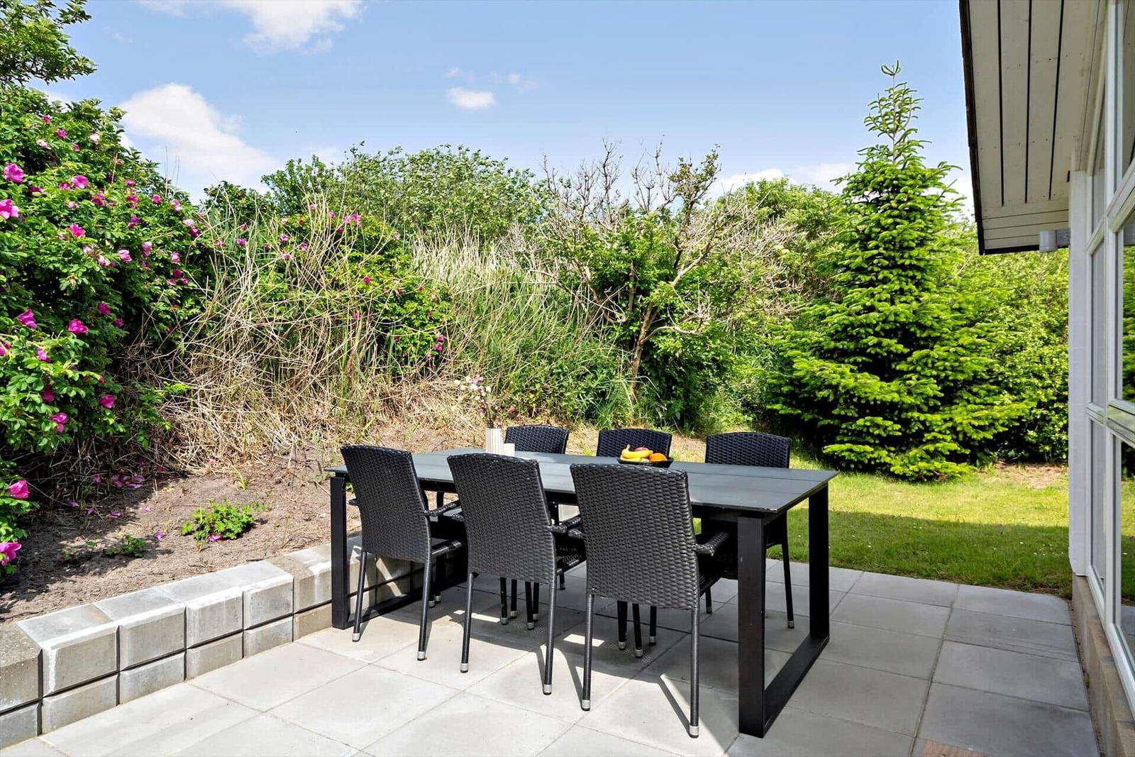 Terrasse mit Esstisch und Stühlen, umgeben von Grün und Blumen.