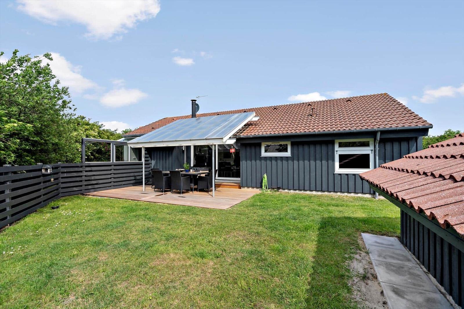 Haus mit Terrasse, Garten und Holzverkleidung unter blauem Himmel.