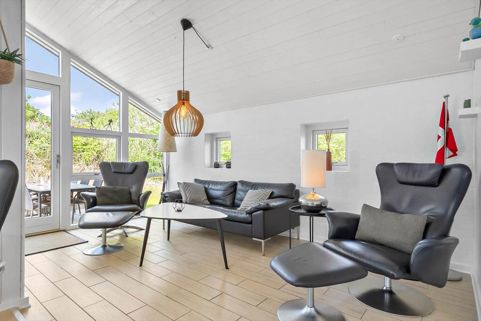 Wohnzimmer mit schwarzen Sesseln, Sofa und großem Fenster zur Terrasse.