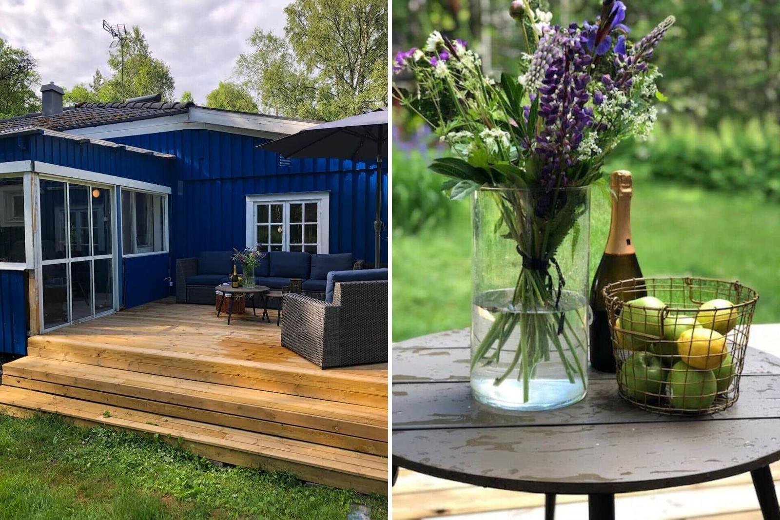 Blauer Holzhaus mit Terrasse und Gartenmöbeln. Tisch mit Blumen, Champagner und Obst.