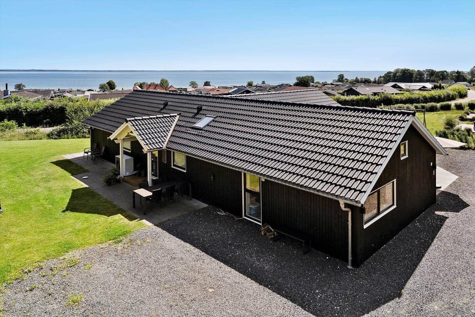 A house with dark siding and roof, surrounded by lawn and water view.