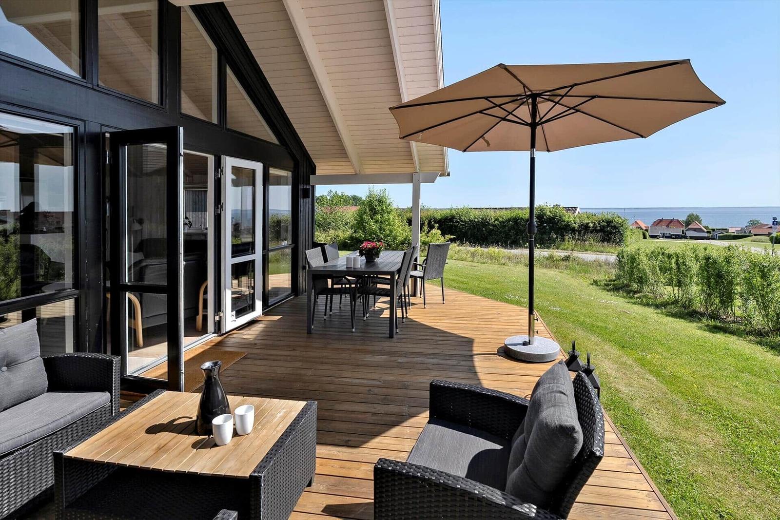 Terrace with seating, table, and umbrella. View of lawn and sea.
