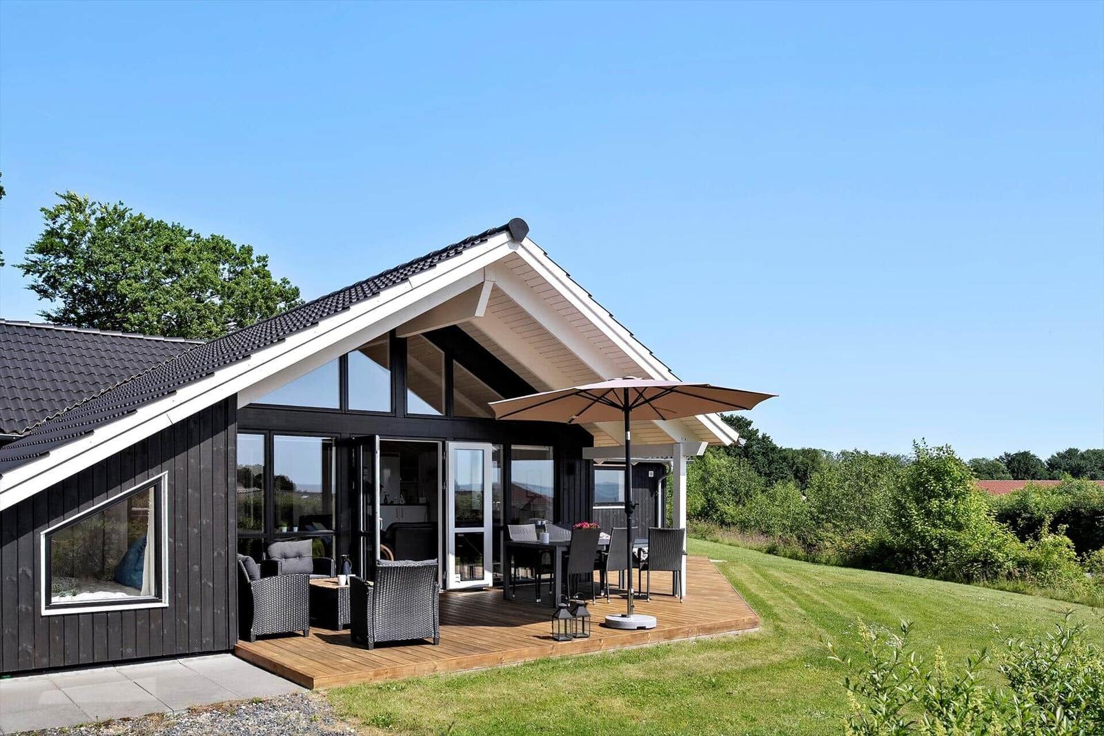 Modern villa with terrace, seating, and view of green landscape.