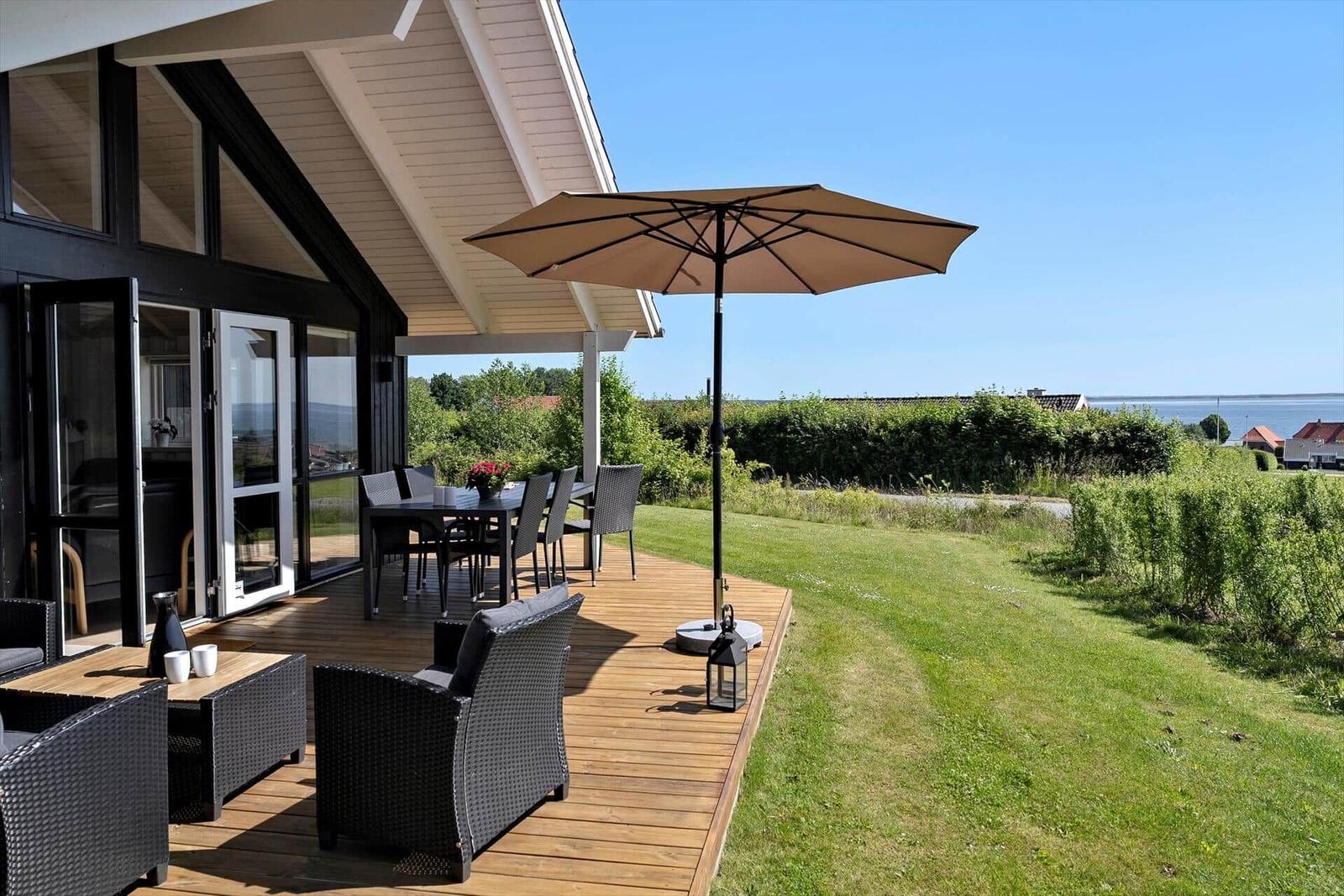 Deck with seating, table, and umbrella. View of greenery and water.