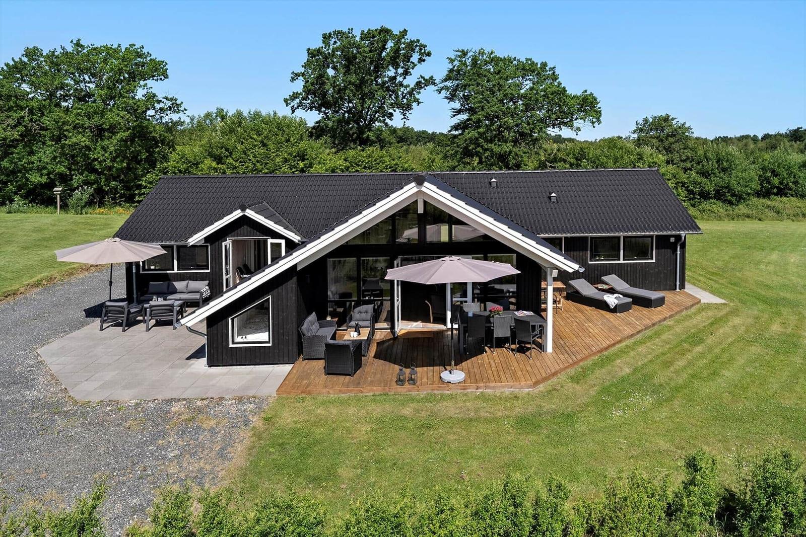 Modern villa with large wooden terrace and garden. Outdoor seating areas with umbrellas.