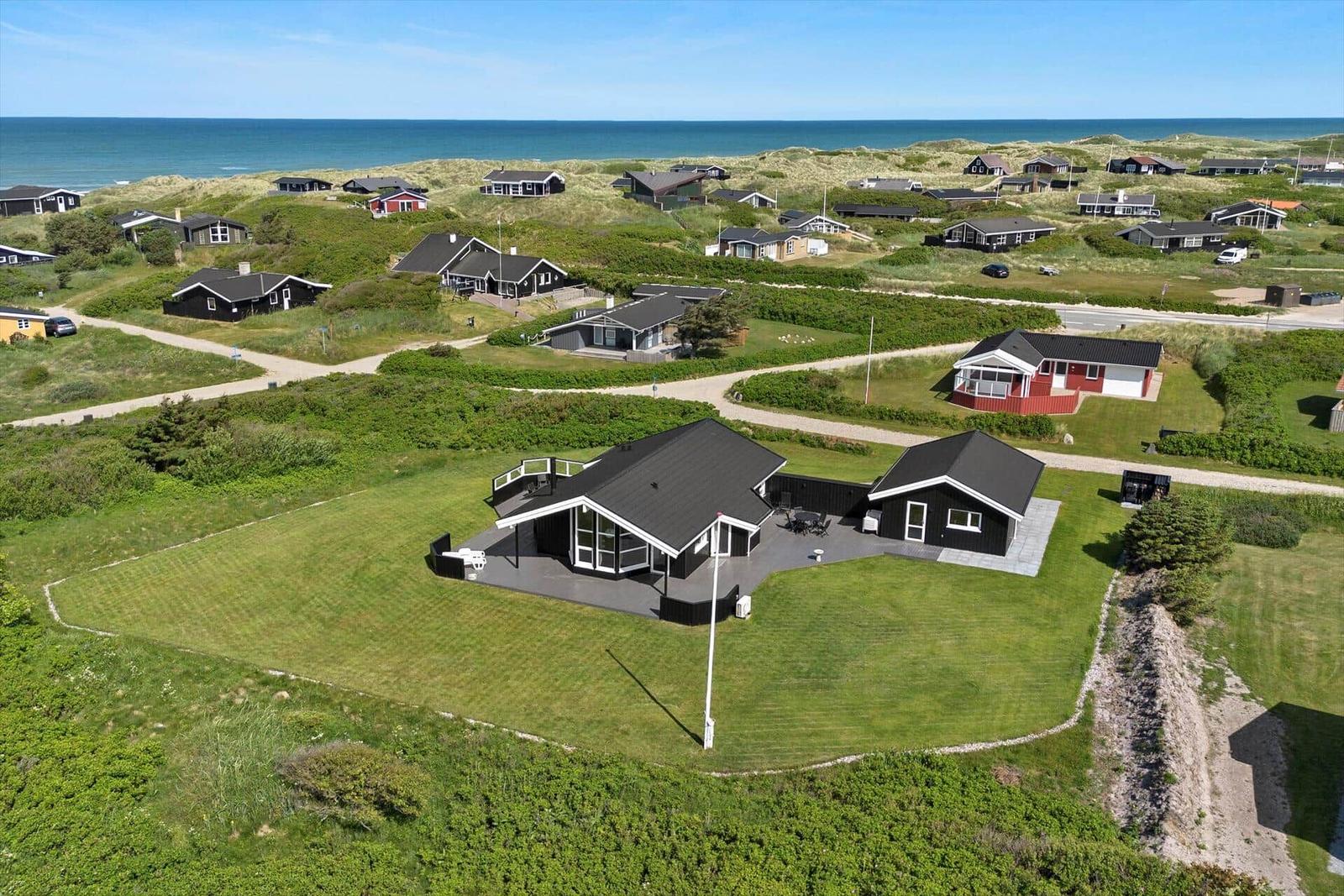 Modernes Haus mit Terrasse auf grünem Grundstück nahe Strand und Dünen.