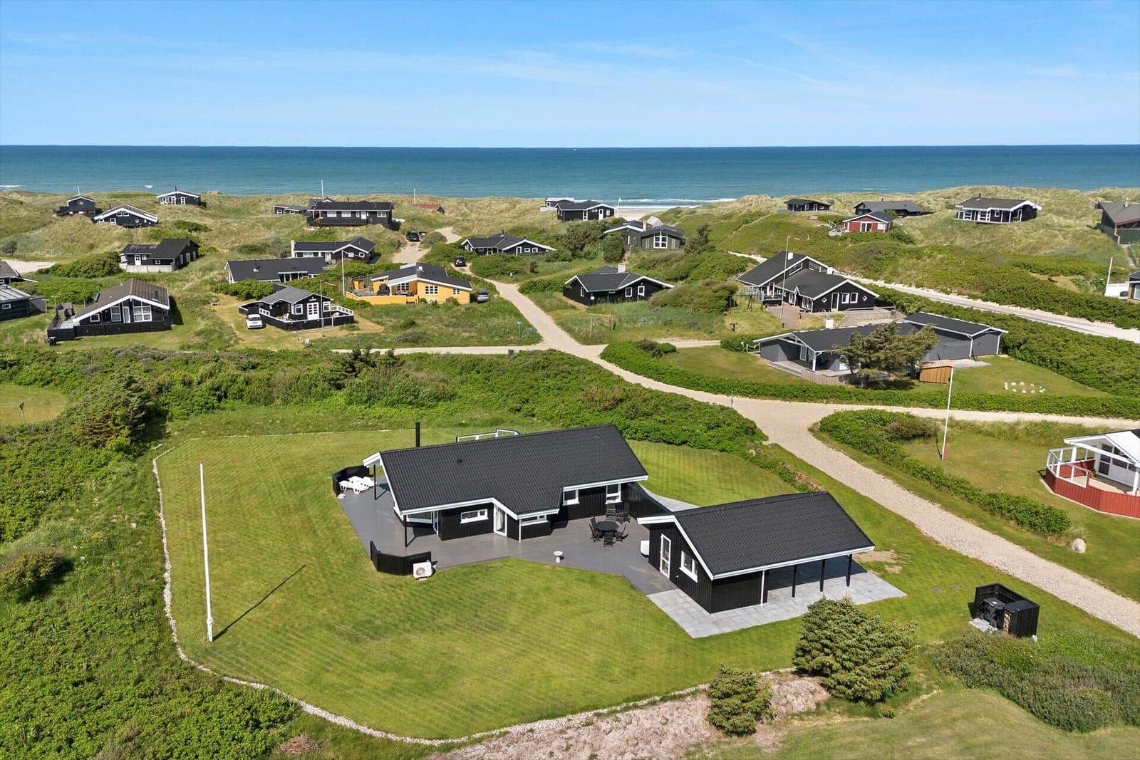 Schwarze Strandhäuser auf grünen Dünen mit Blick auf das Meer.