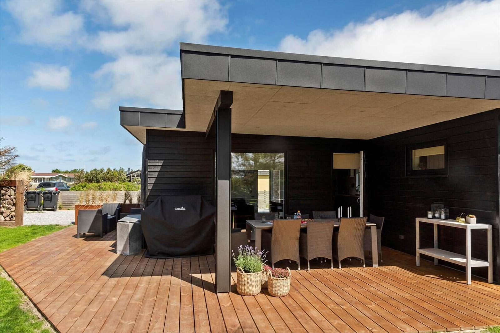 Terrasse mit Tisch, Stühlen und Grill unter modernem Überdachungsbereich.