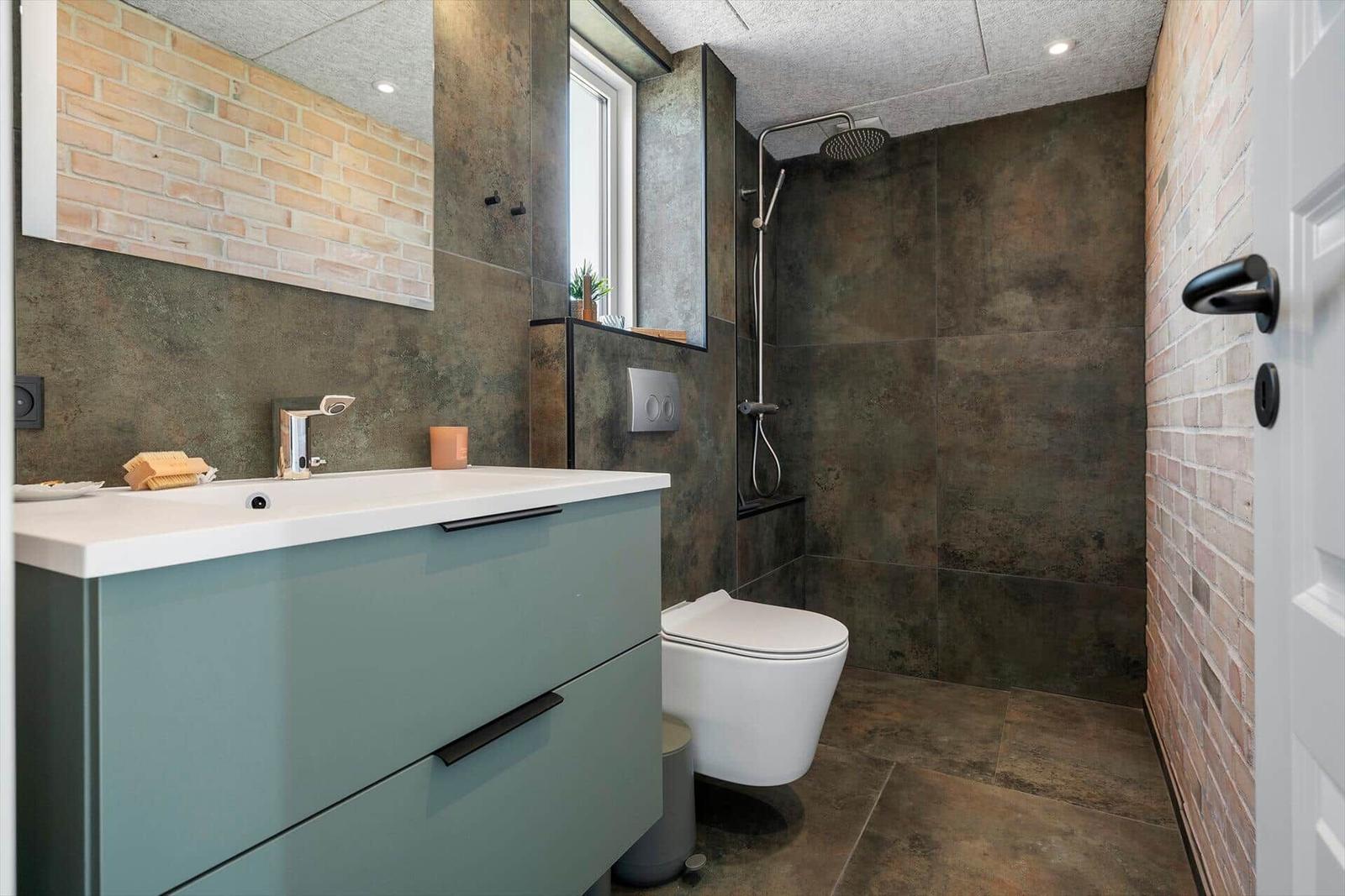 Badezimmer mit Dusche, Waschbecken und Toilette. Wandverkleidung aus Ziegel und Stein.