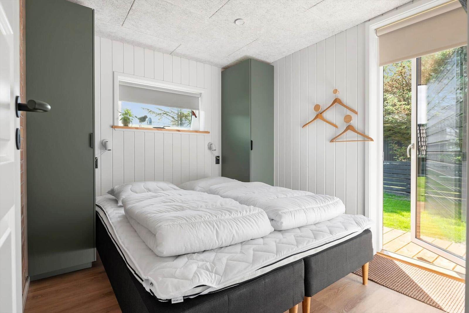 Schlafzimmer mit Doppelbett, Fenster und Glastür zum Garten.