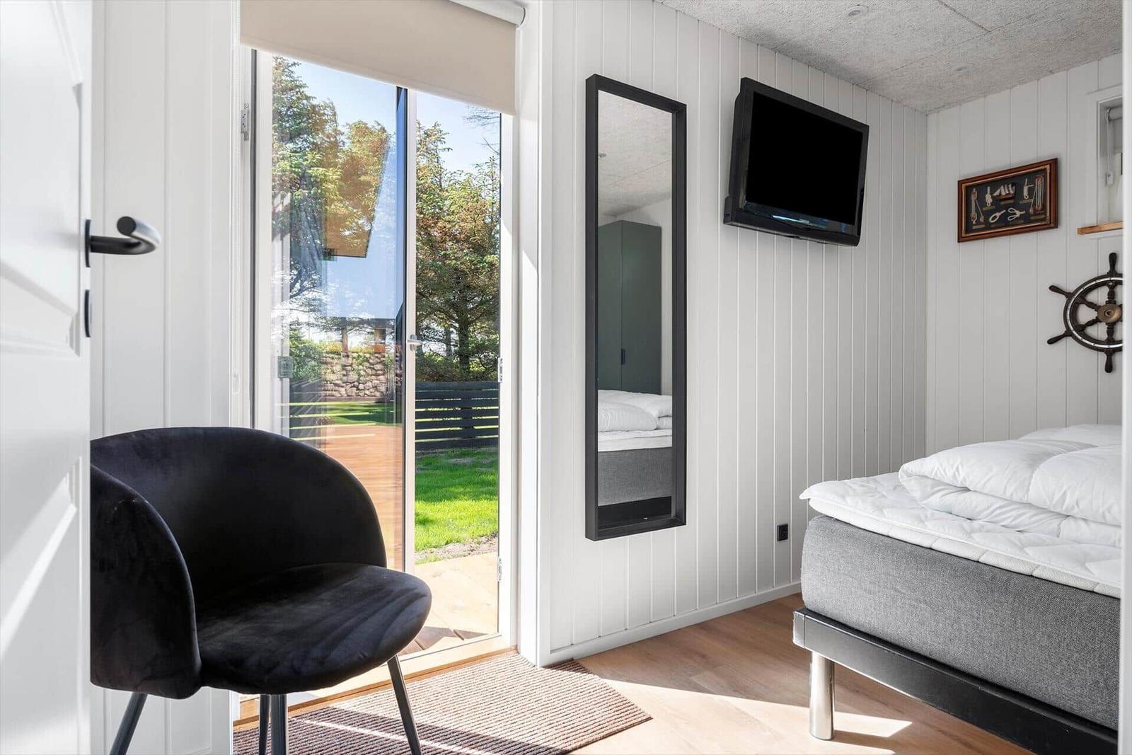 Schlafzimmer mit Bett, Spiegel und TV. Durchgang zur Terrasse mit Garten.