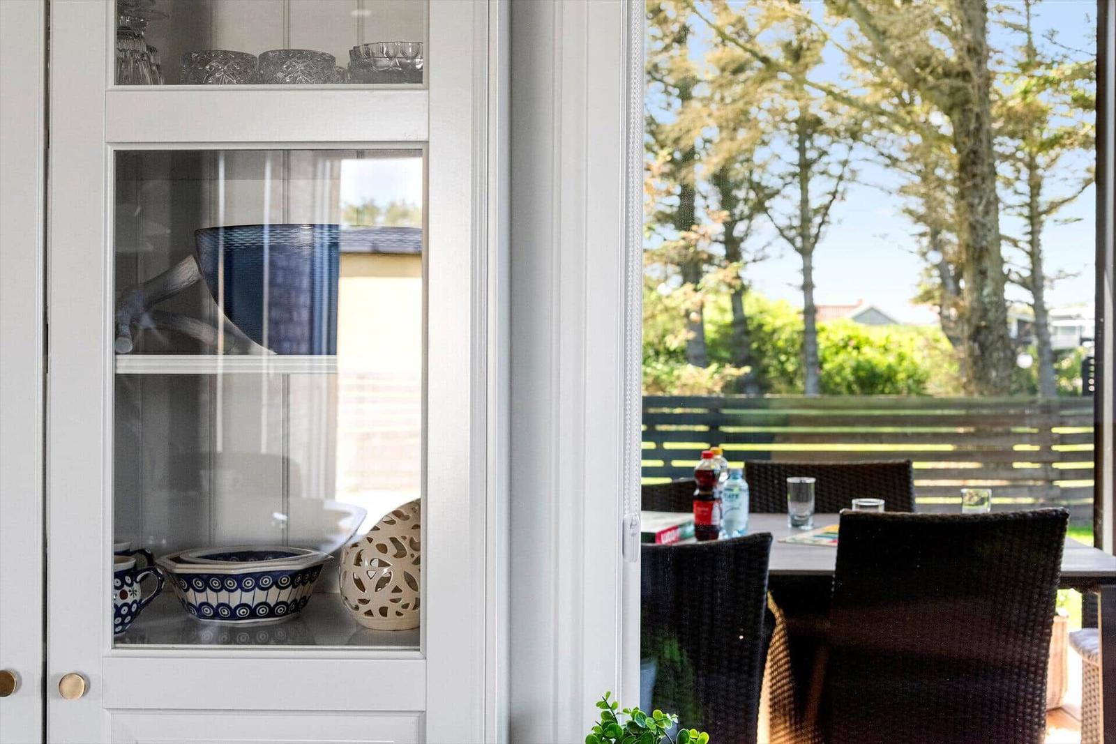 Weißer Schrank mit Geschirr, Blick auf Terrasse mit Tisch und Stühlen.