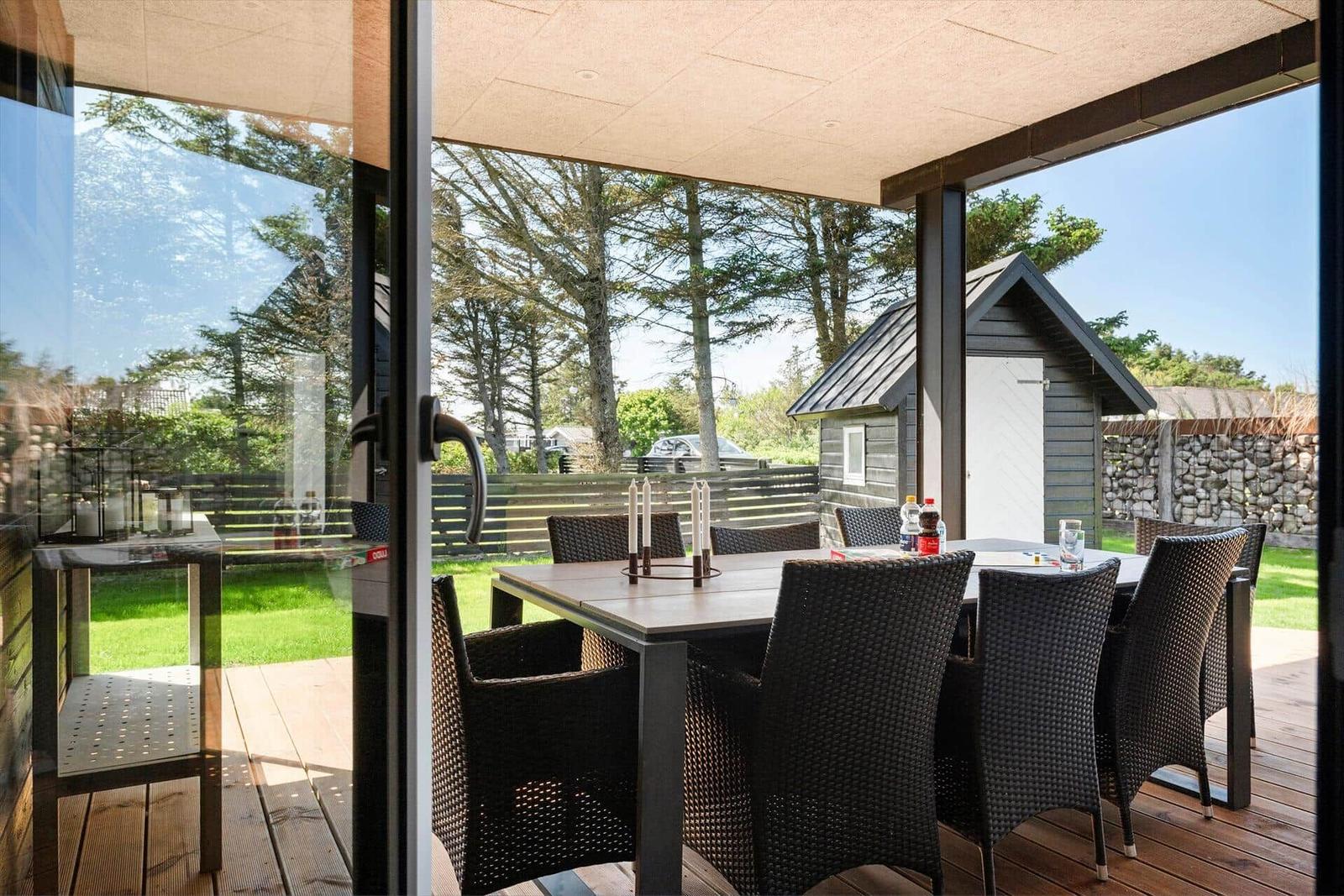 Terrasse mit Tisch und Stühlen, Blick auf Garten und Holzhaus.