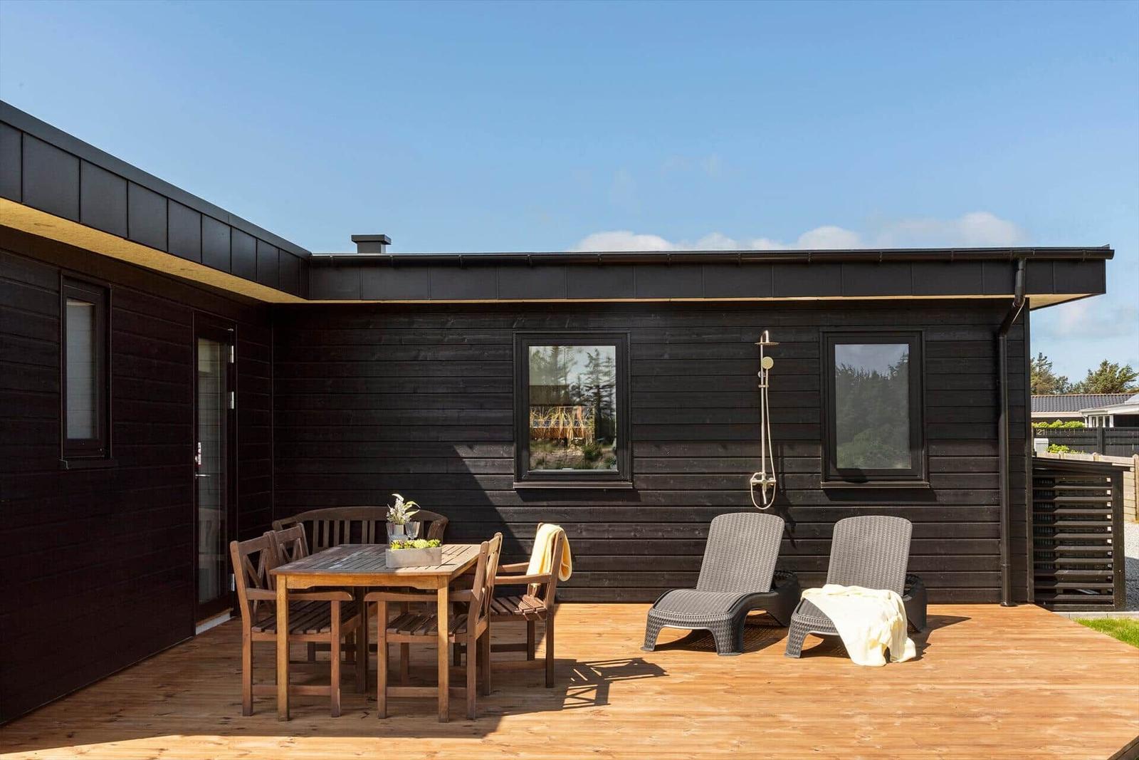 Terrasse mit Tisch, Stühlen und Liegen vor einem dunklen Holzhaus.