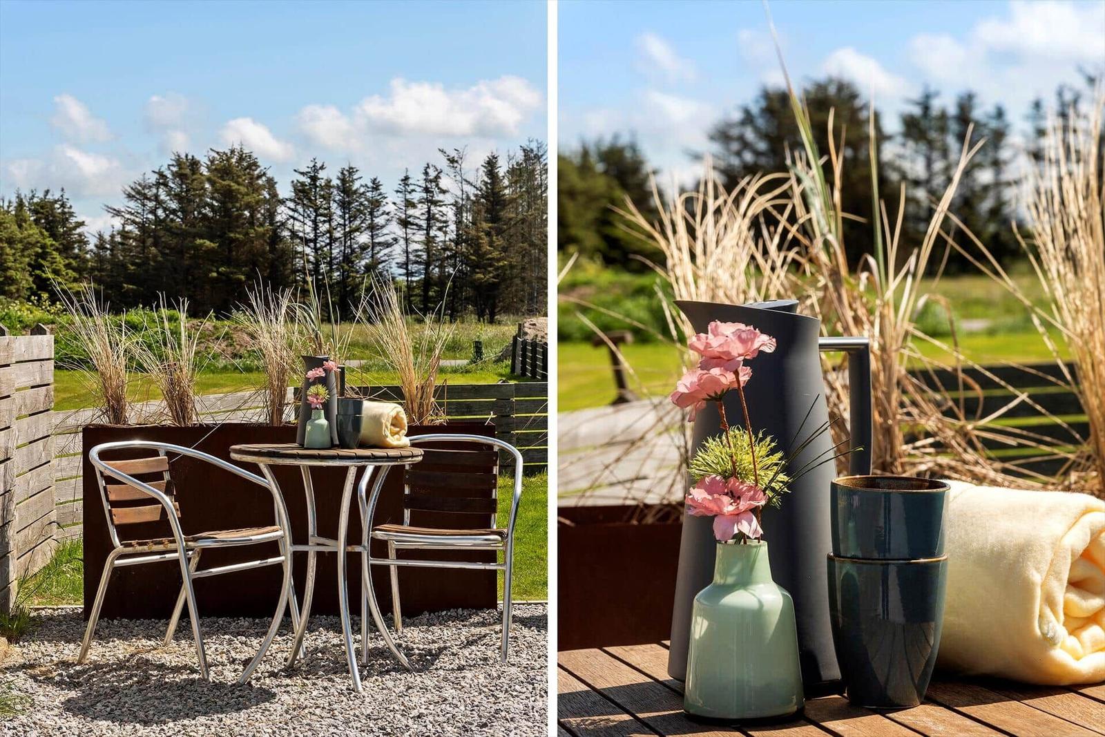 Außenbereich mit Tisch, Stühlen und Blumen. Holz- und Steinflächen. Grünflächen und Bäume im Hintergrund.